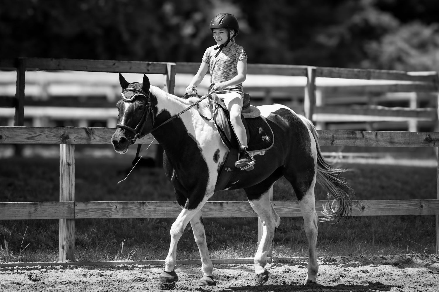 A young rider on a spotted black and white horse practices in an outdoor riding arena at sunset.