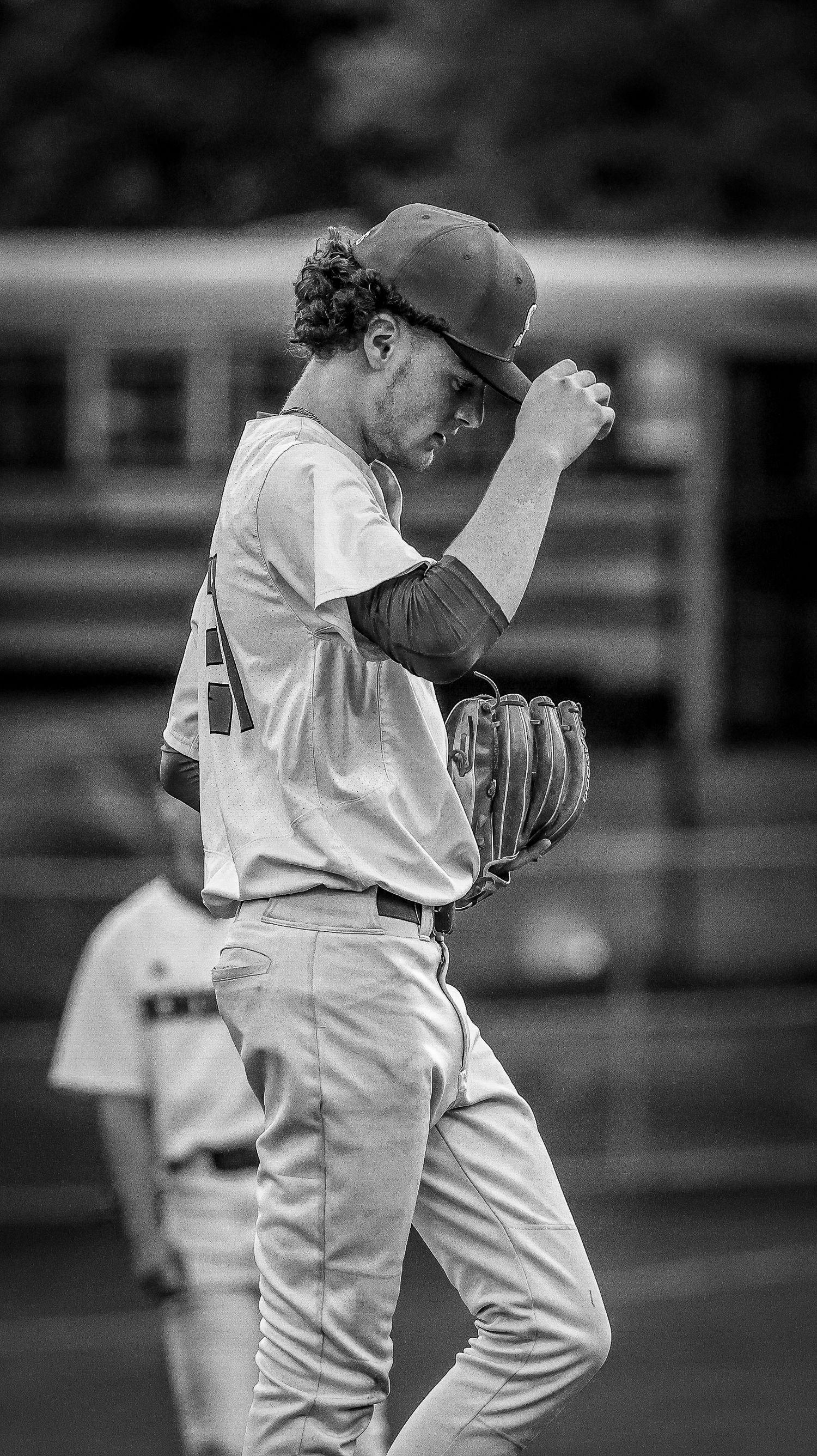 A baseball player in a light uniform shows signs of frustration during a game in a black and white photograph.