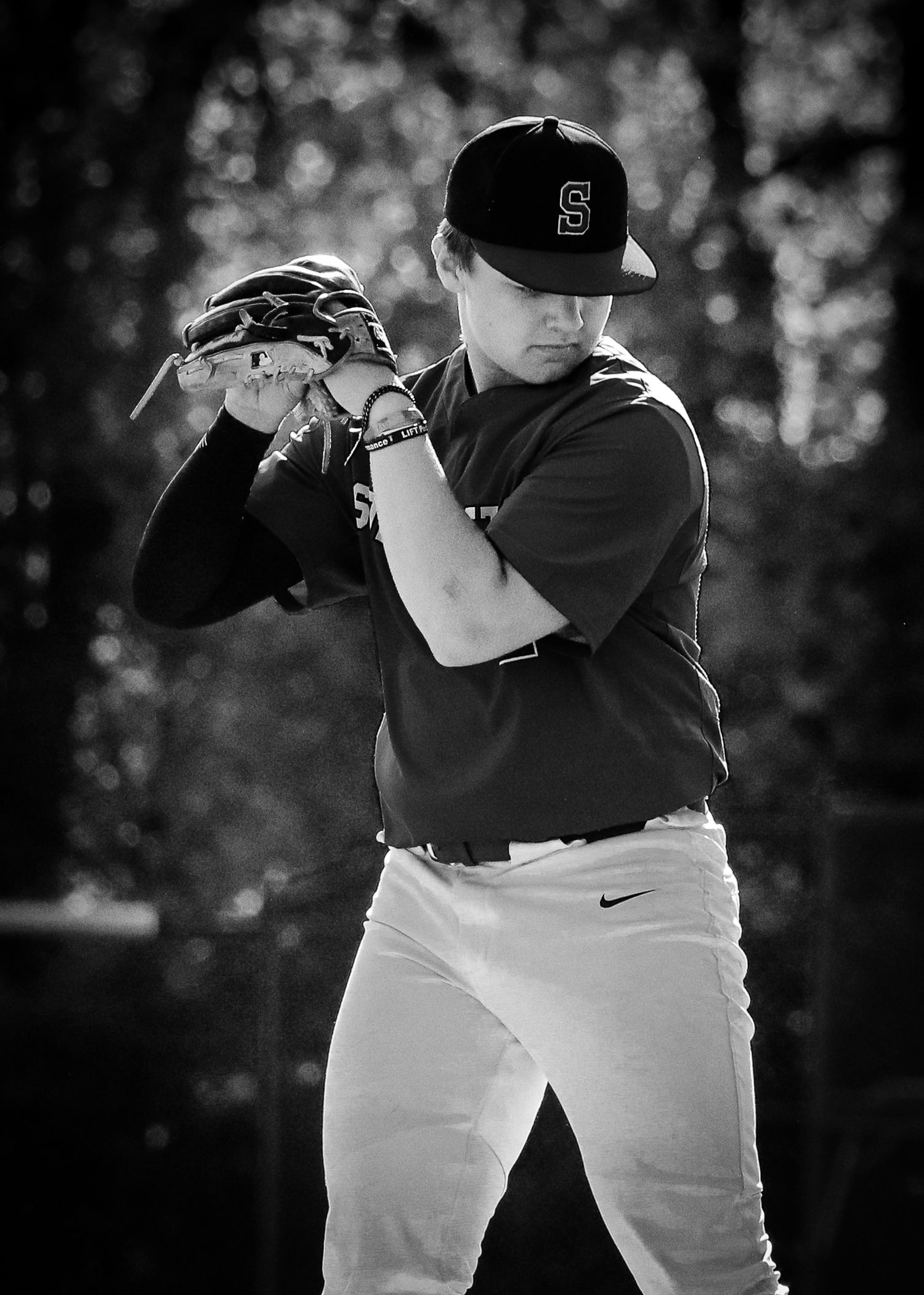 Black and white photo of a baseball player in uniform wearing hat and glove in pitching windup position.
