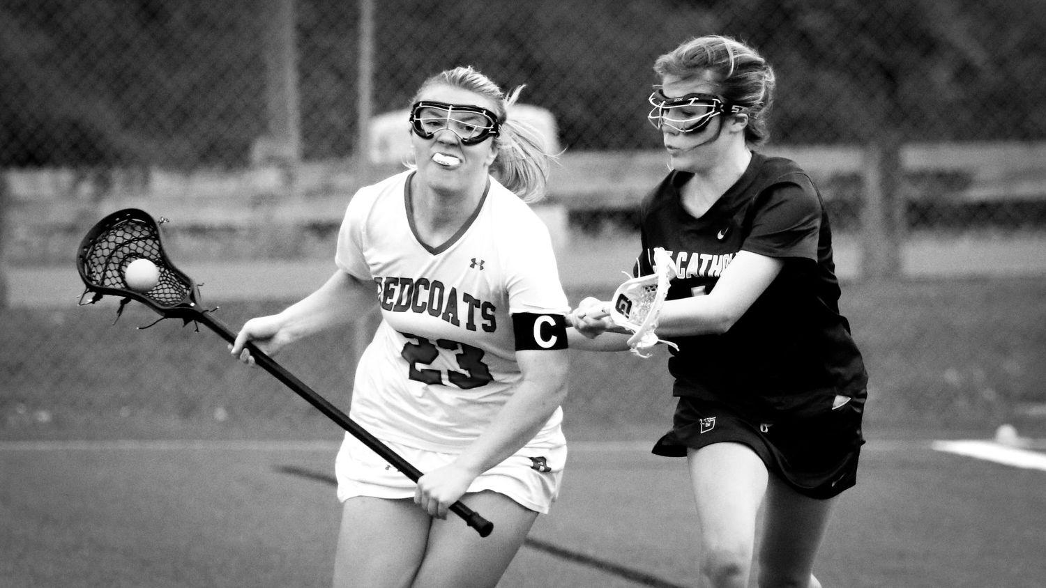 A black and white photo showing athletic players on a lacrosse field during a competitive match.
