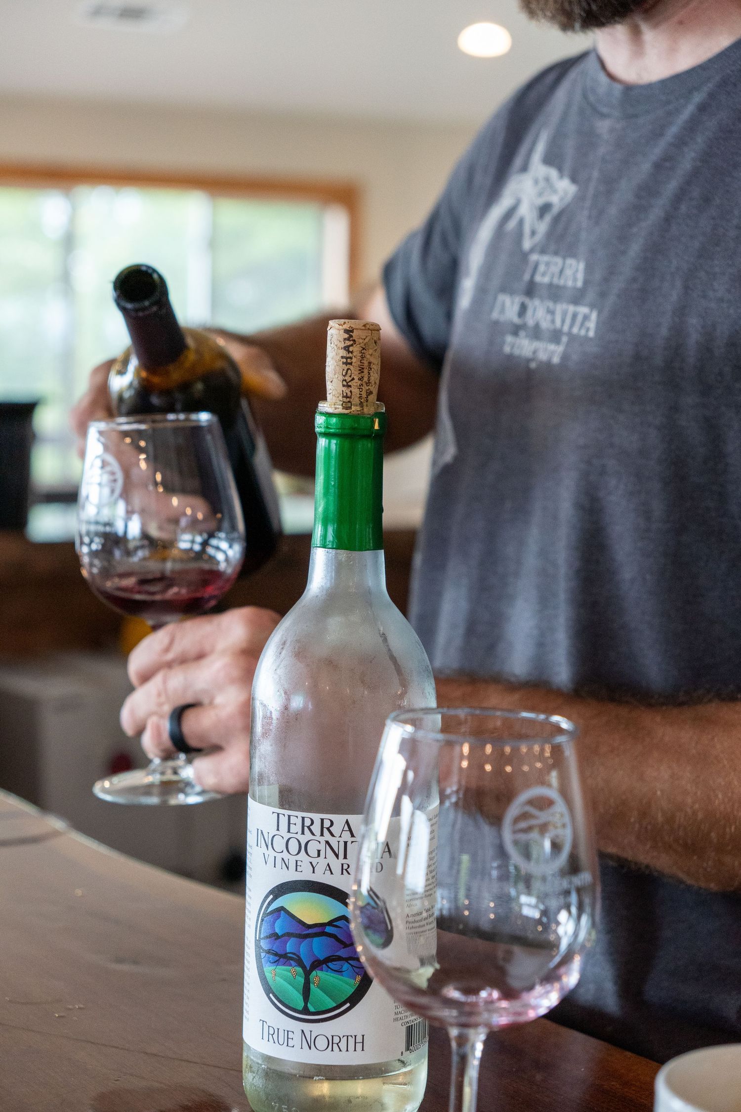 A man pours a glass of wine into a wine glass with a bottle of wine in front of him.
