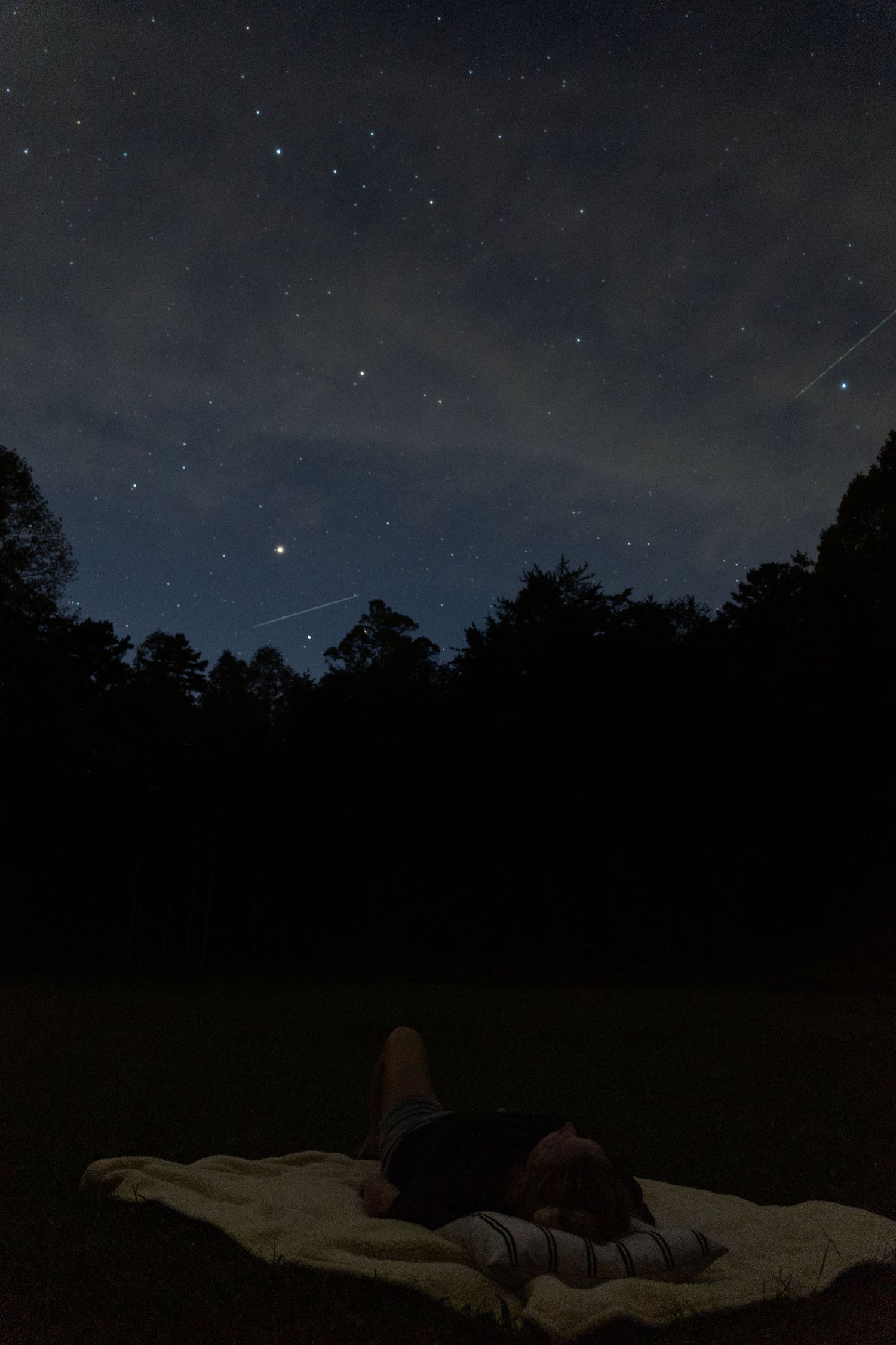 A person lays on a blanket while stargazing at a vacation rental in the mountains