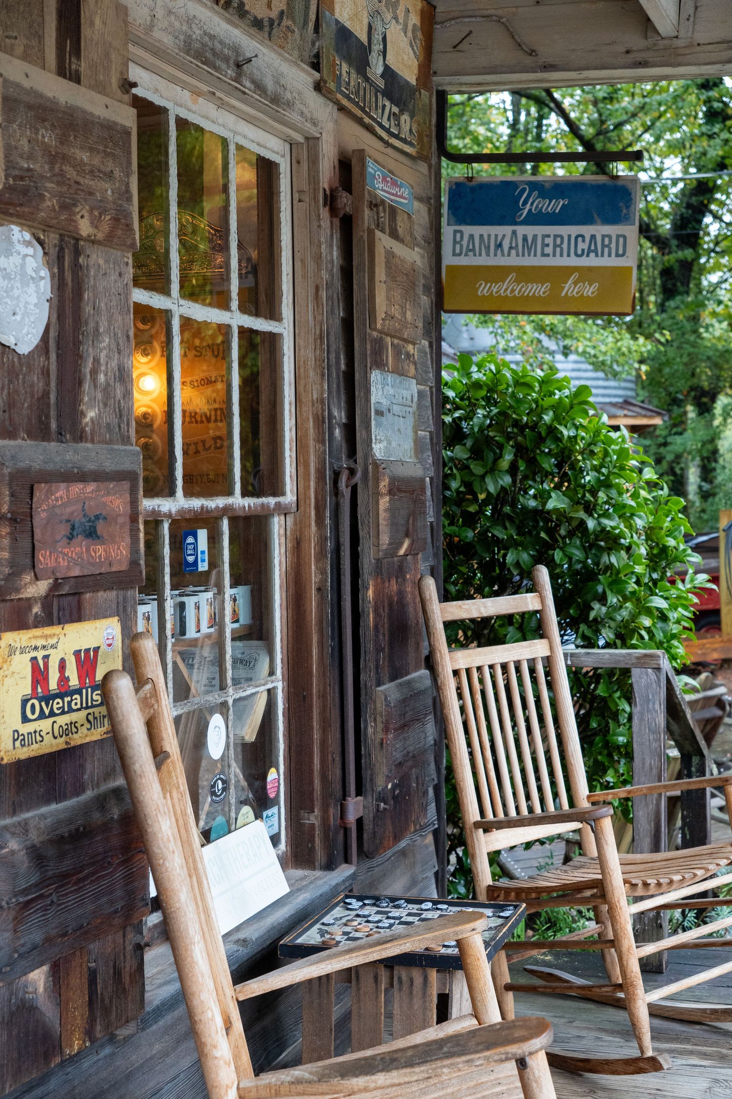 Two old-timey rocking chairs rest against a log building with a classic checker game between them inspiring nostalgia