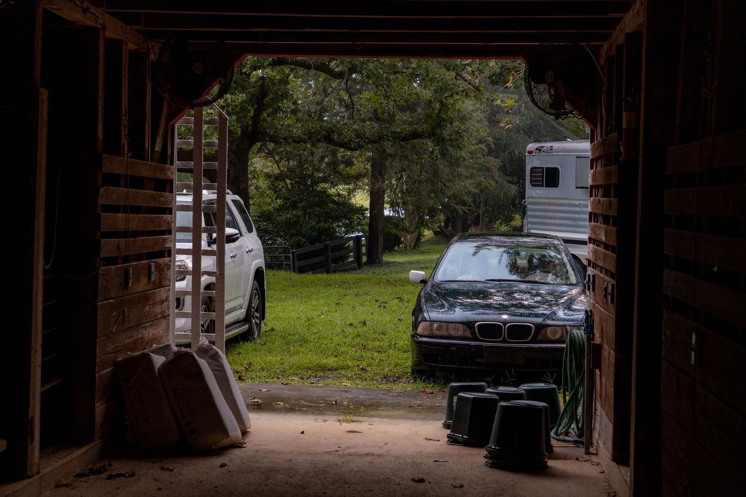 View from inside a barn looking out at a black BMW car parked on grass inspiring farm scenery