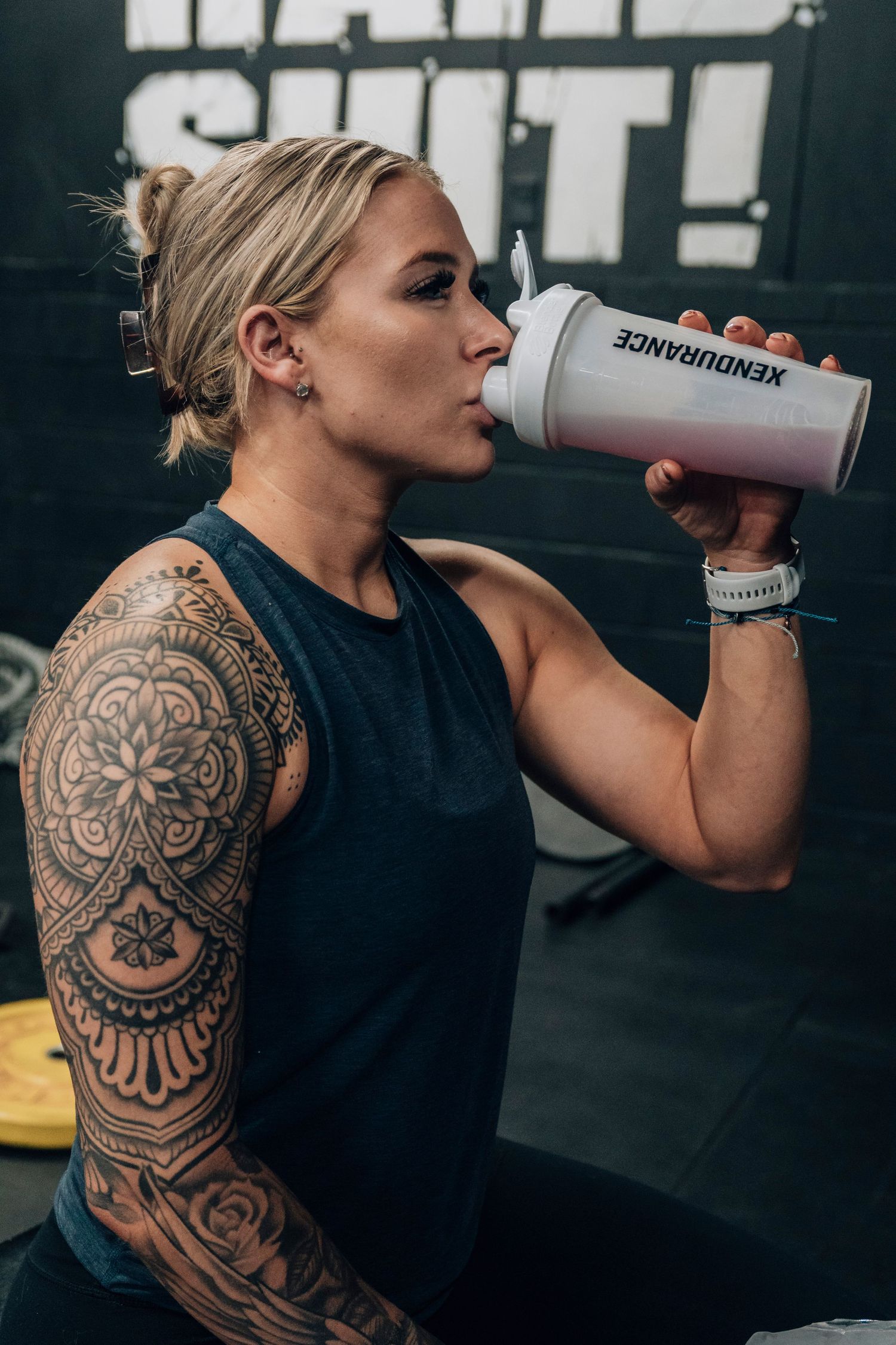 Athlete with detailed arm tattoo drinking from gray water bottle during gym session.