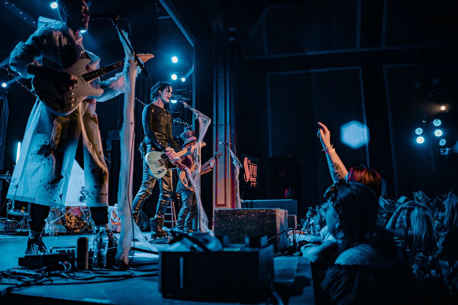 Wide shot of band performing on dark stage with blue spotlights and string lights overhead.