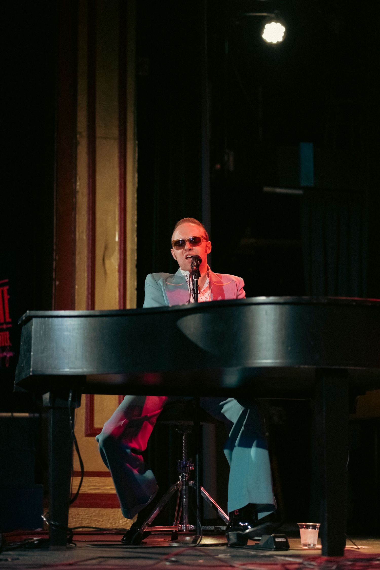 A performer in formal attire playing piano on a dark stage with red accents.