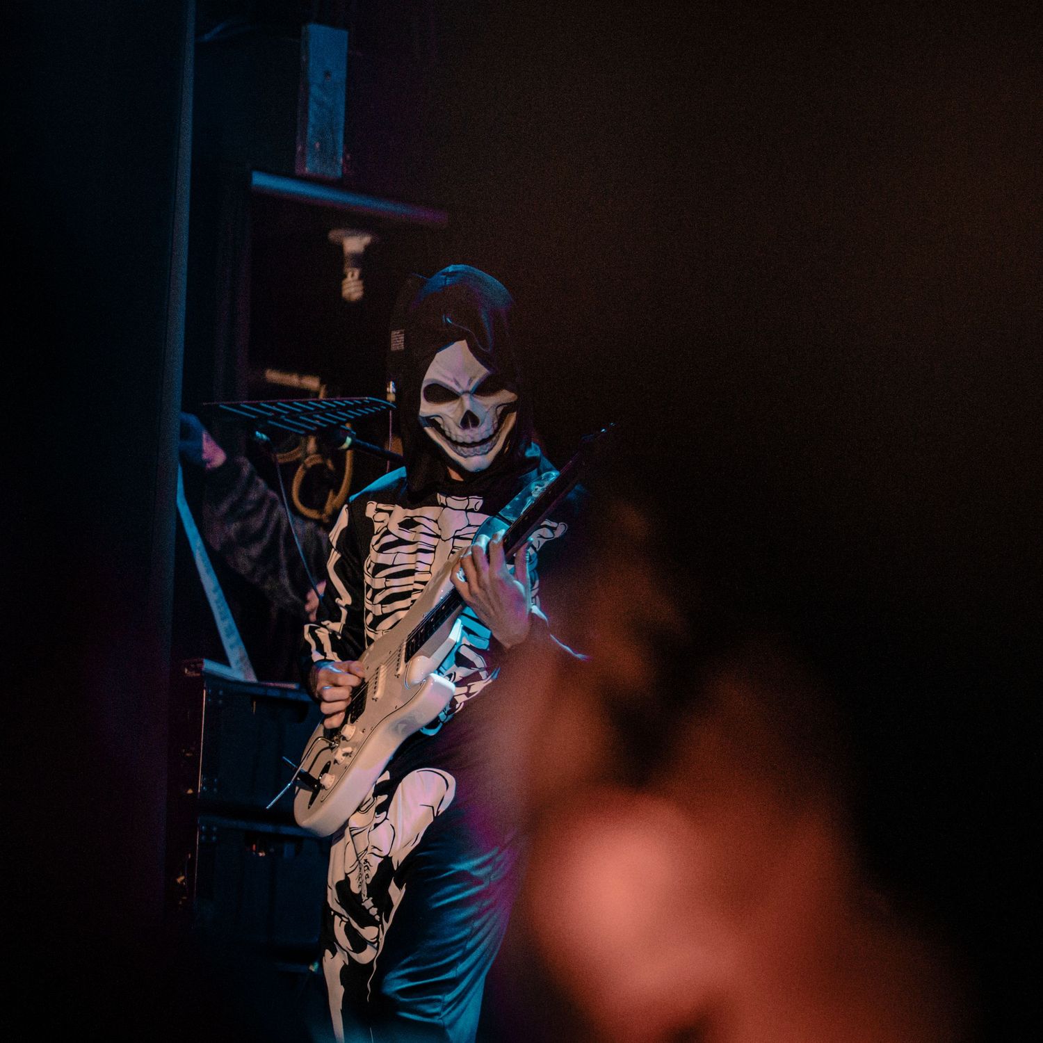 Musician performs with guitar in dark venue with dramatic backlighting.