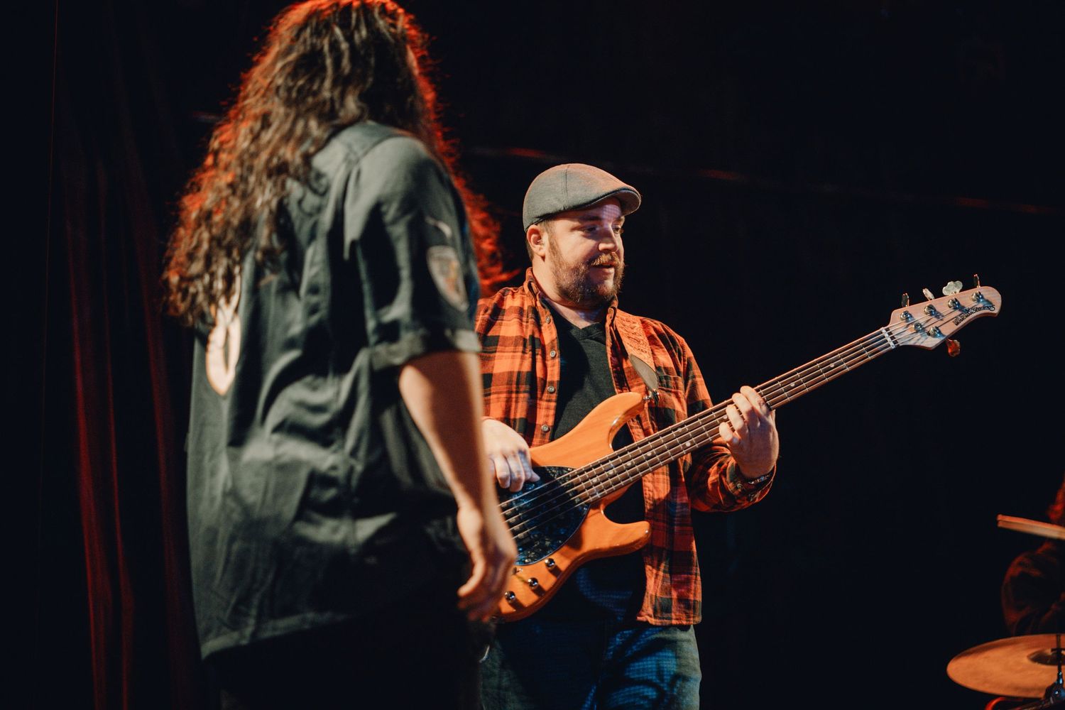 Musicians perform with guitars on stage under warm lighting.