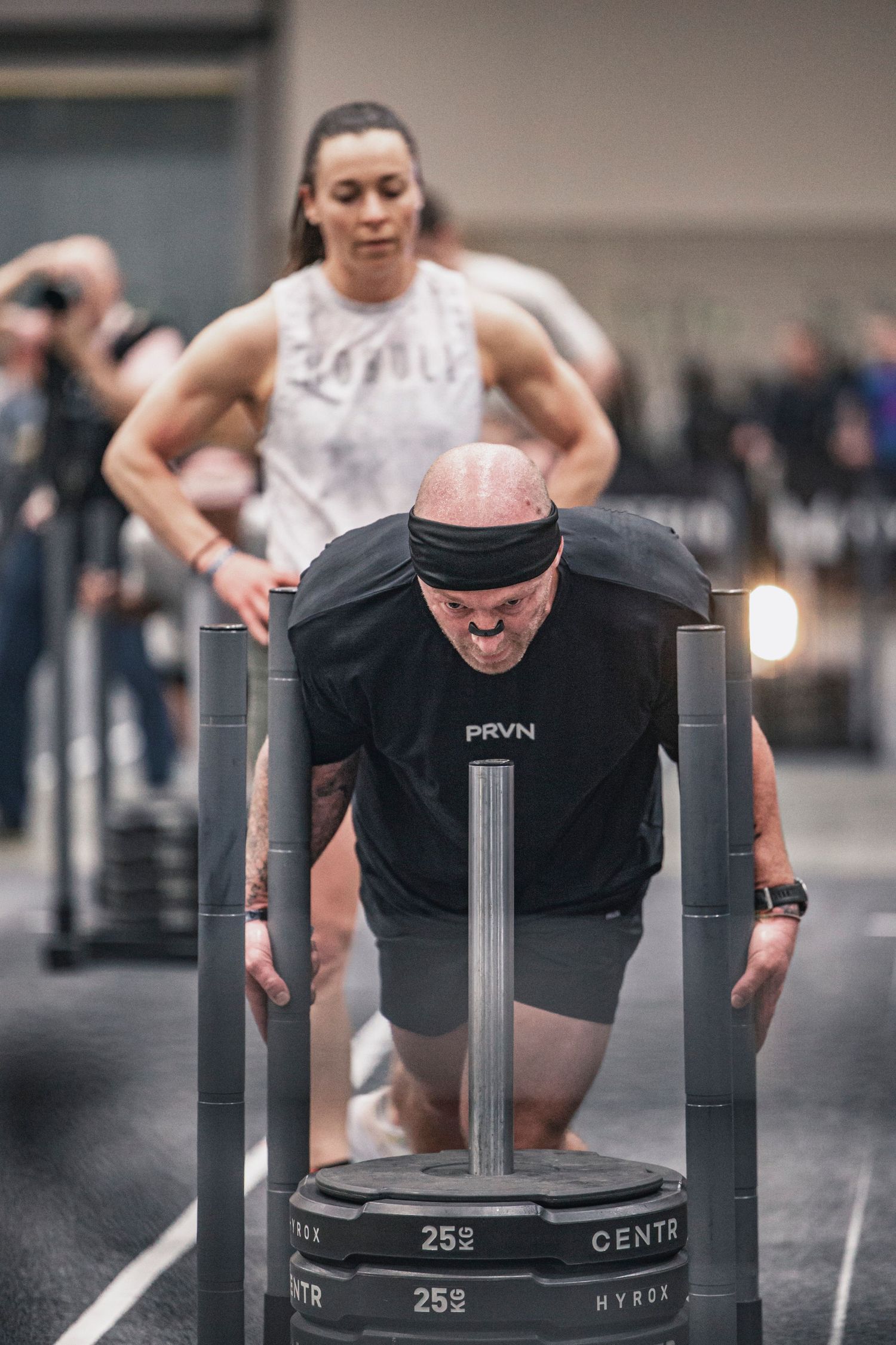 Athletes pushing weighted sleds across a gym floor during competition.
