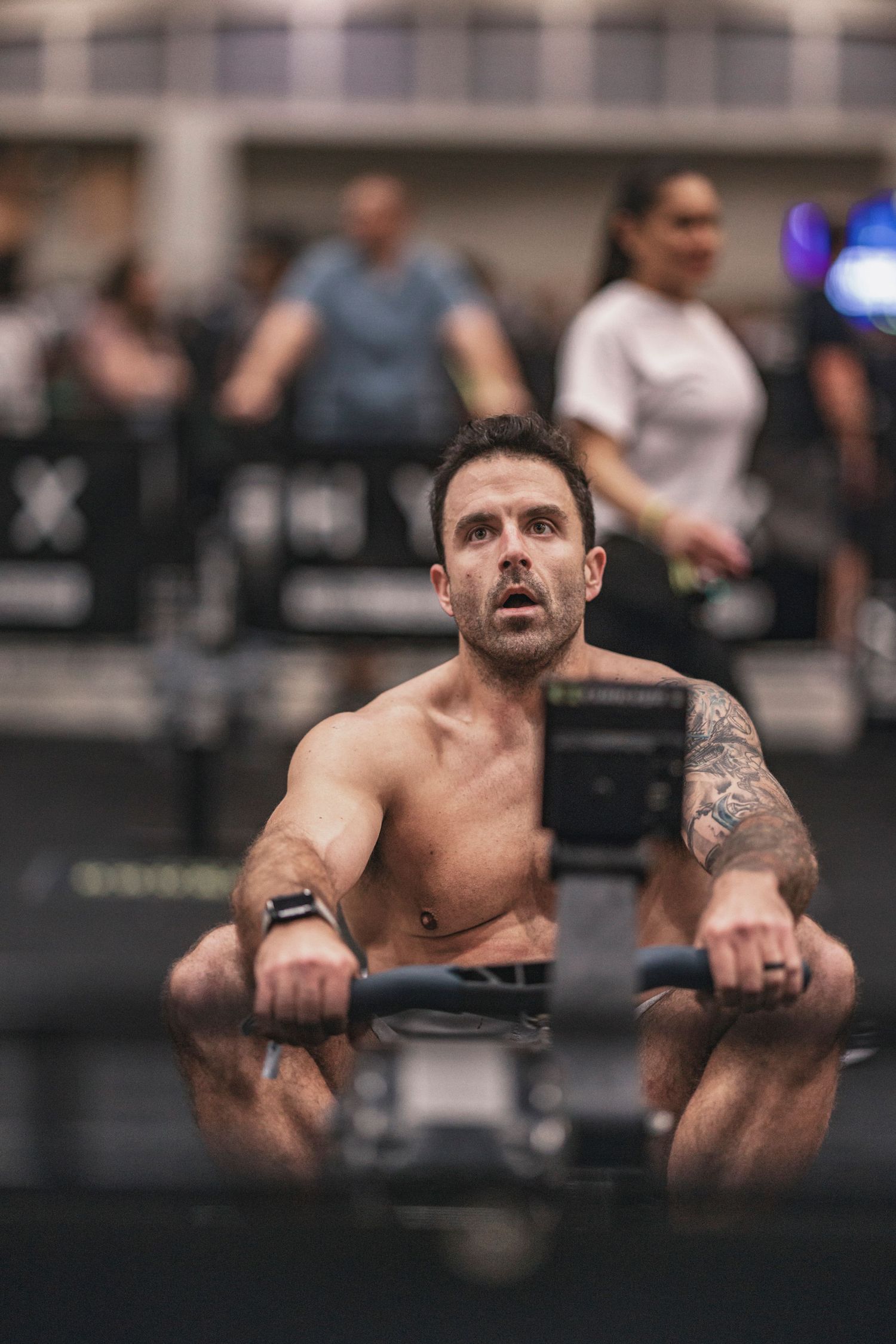 Muscular athlete performing intense rowing exercise on gym equipment.