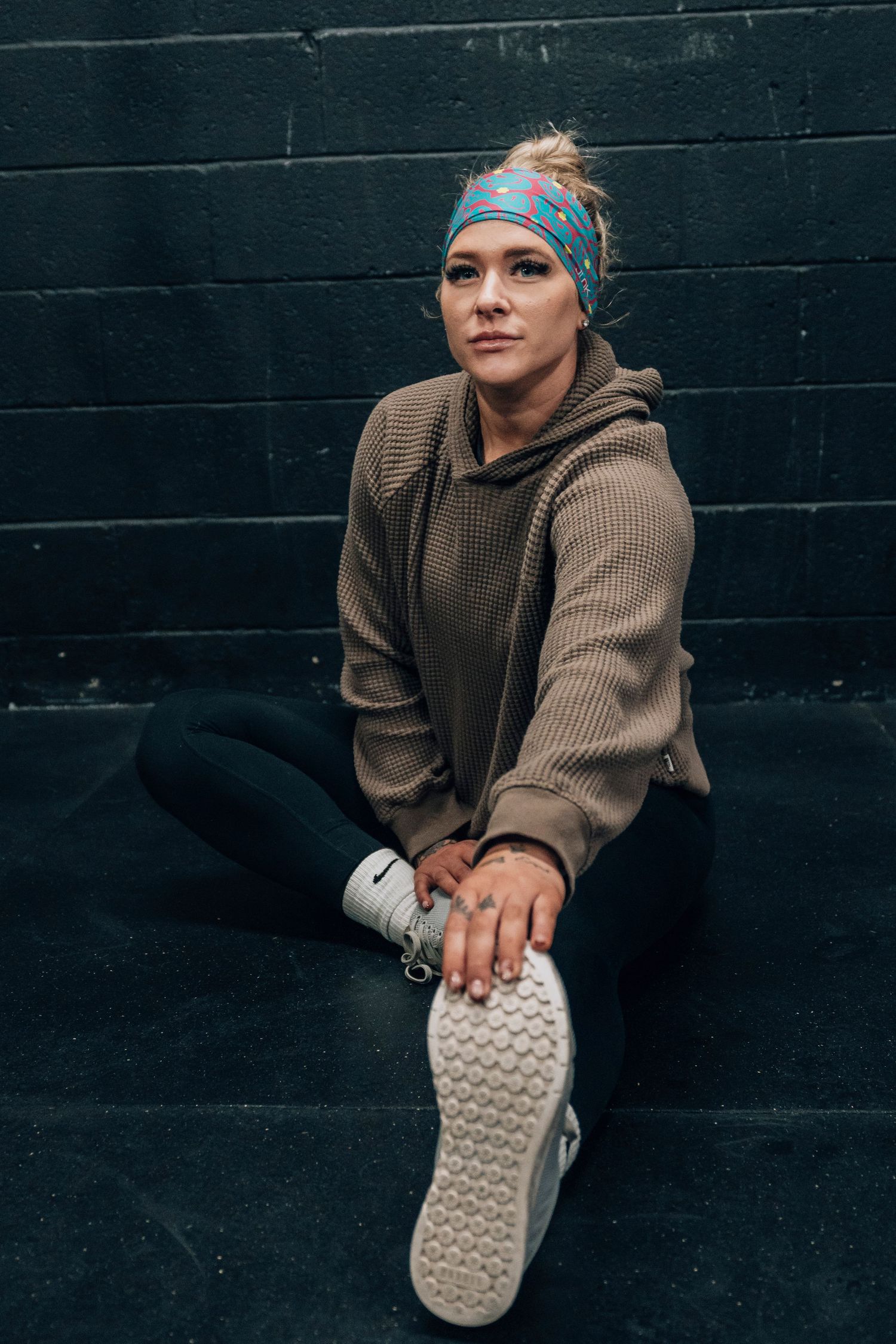 Person in brown sweater and headband stretches against black wall showing shoe sole.