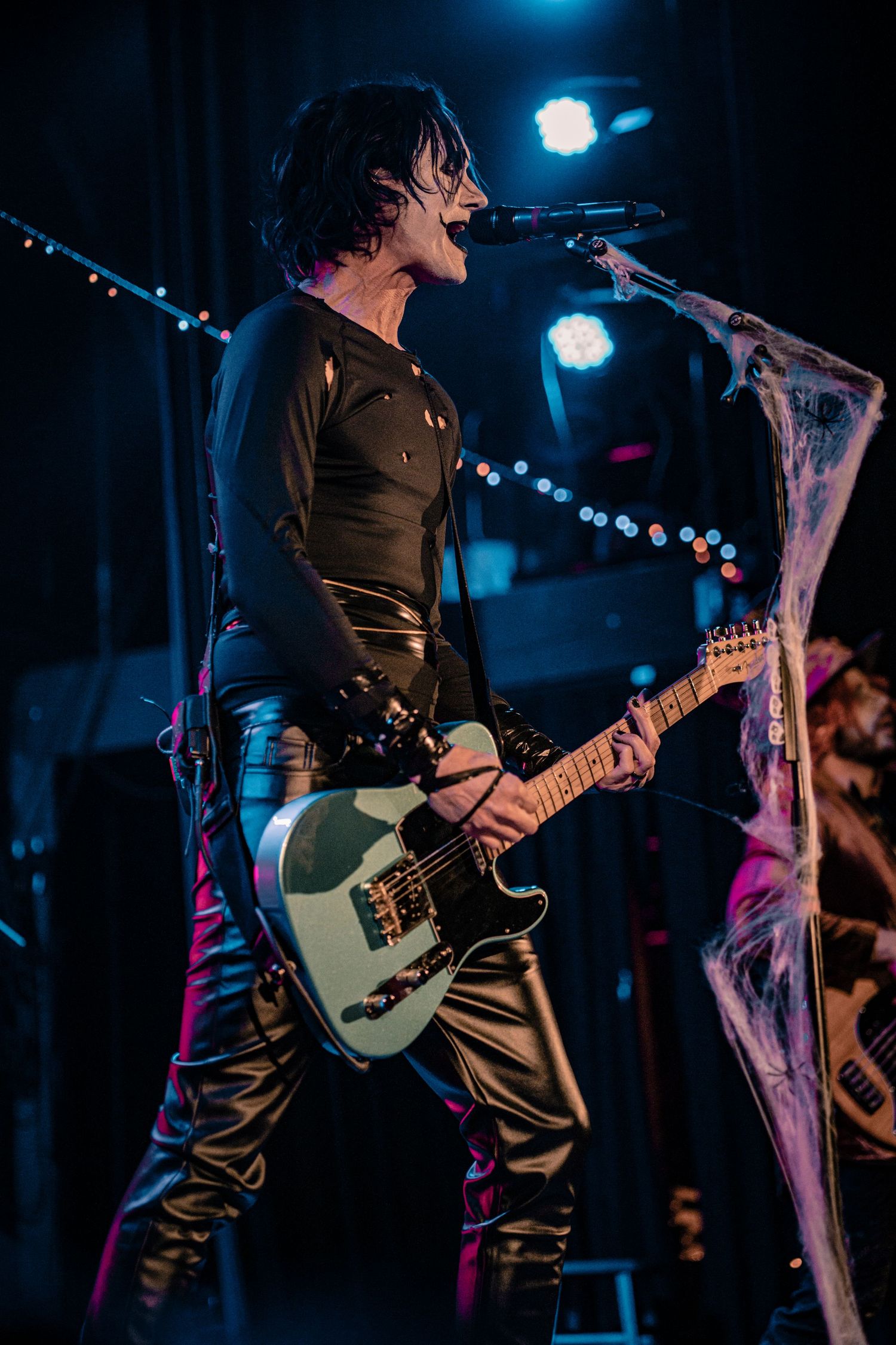 Guitarist plays electric bass guitar on darkened stage with blue accent lighting.