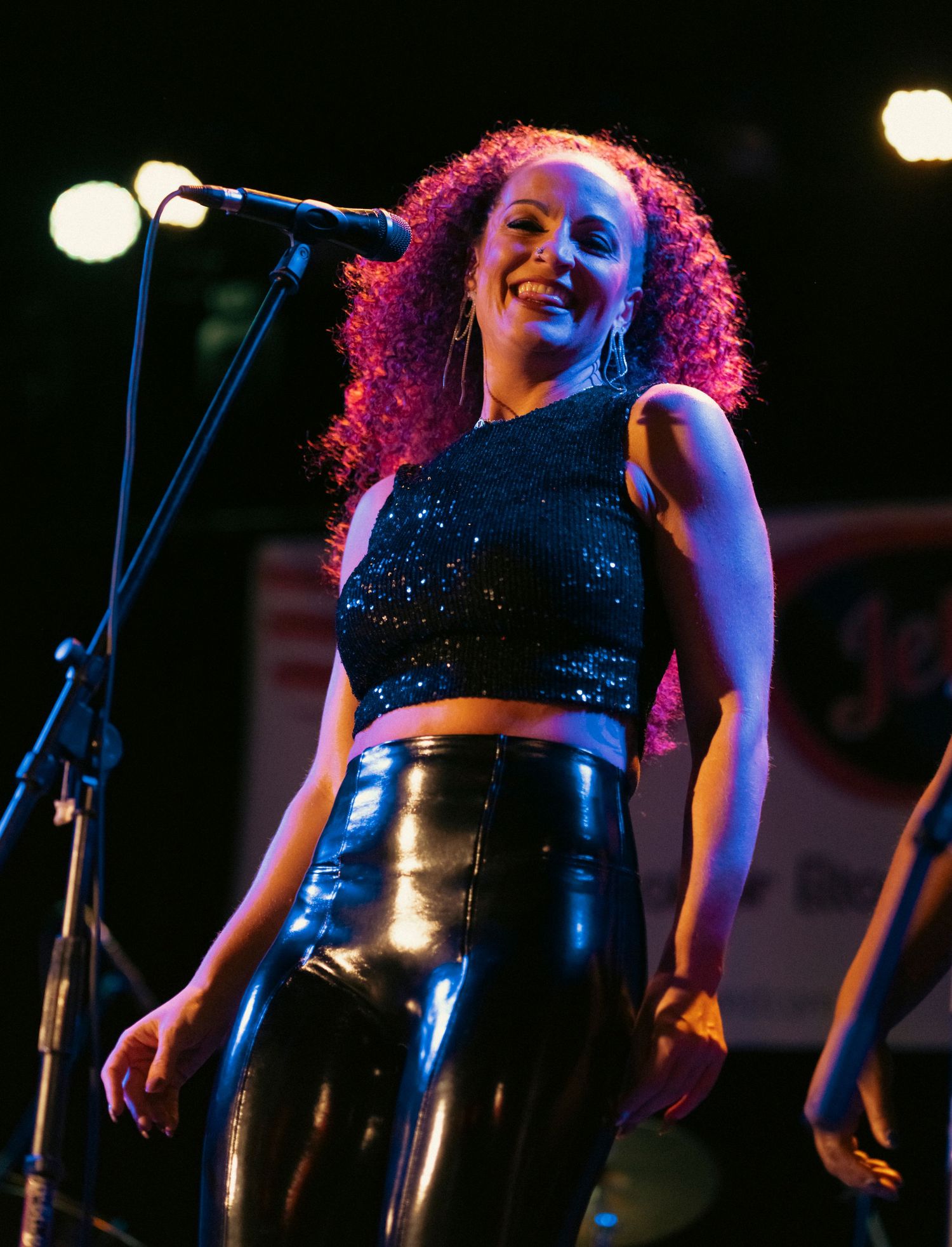 A performer in a sparkly black top illuminated by stage lights during a concert performance.