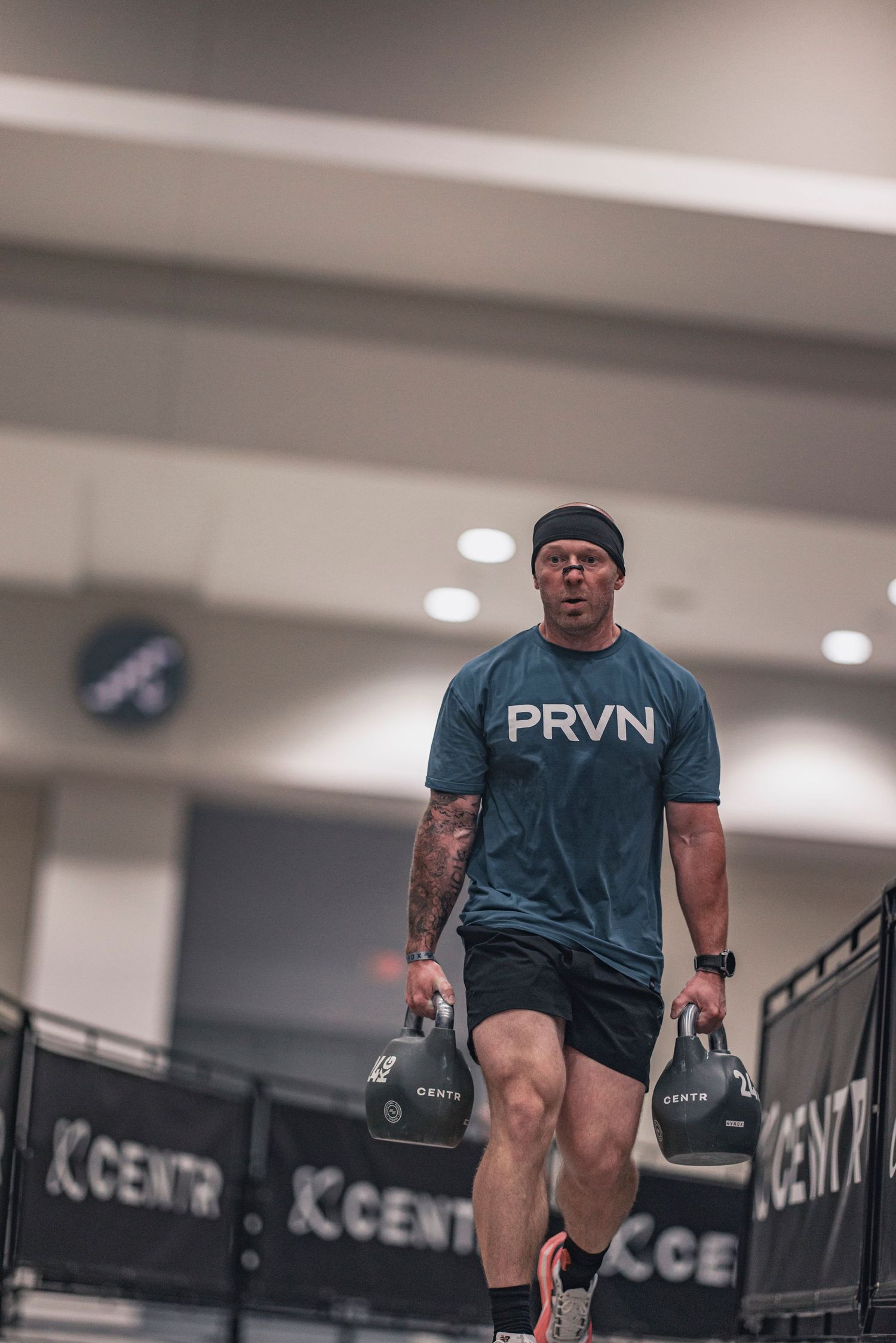 Athlete performing dumbbell exercises in indoor training facility with PRVN shirt.