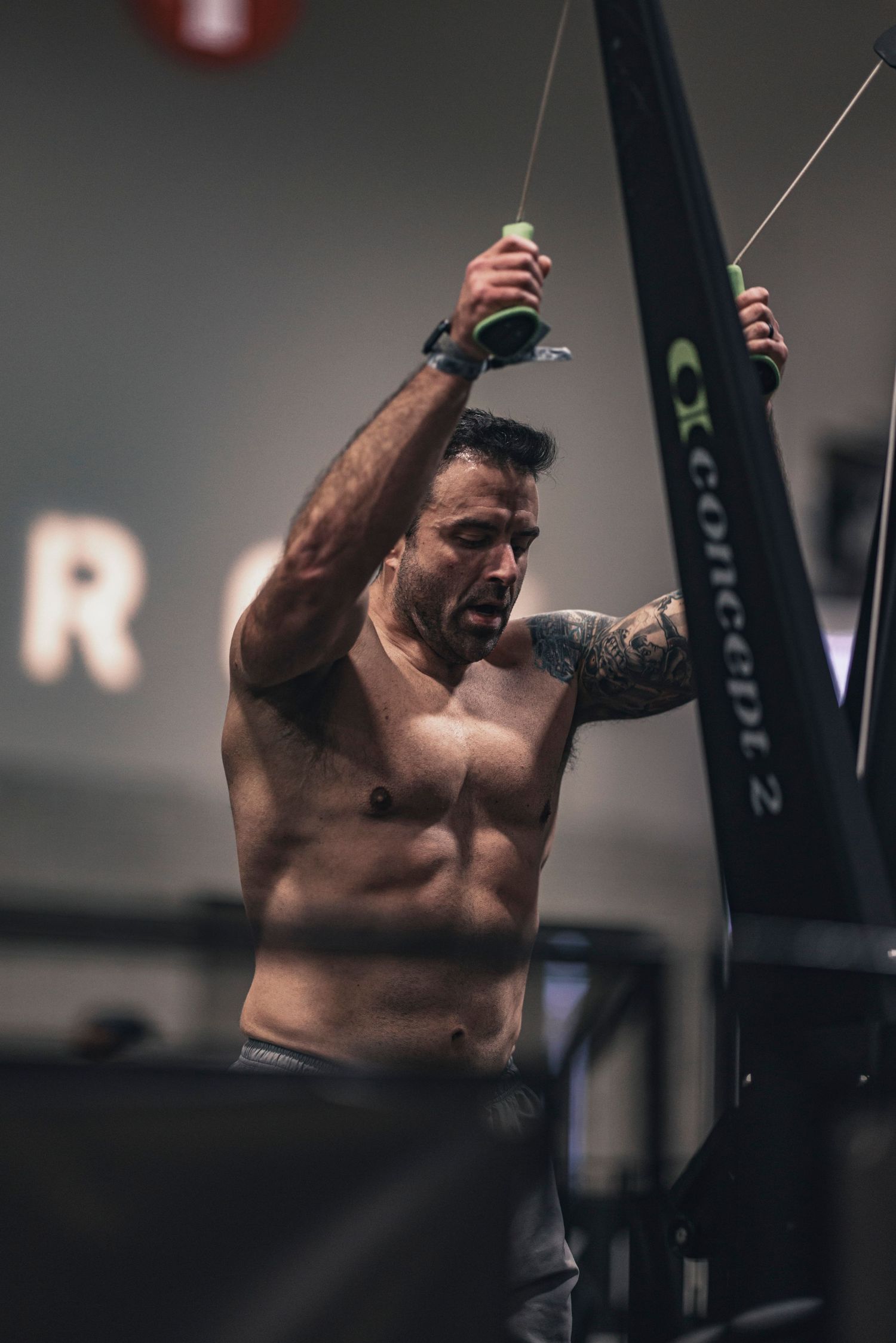 Shirtless athlete performing overhead cable exercises in a gym setting.
