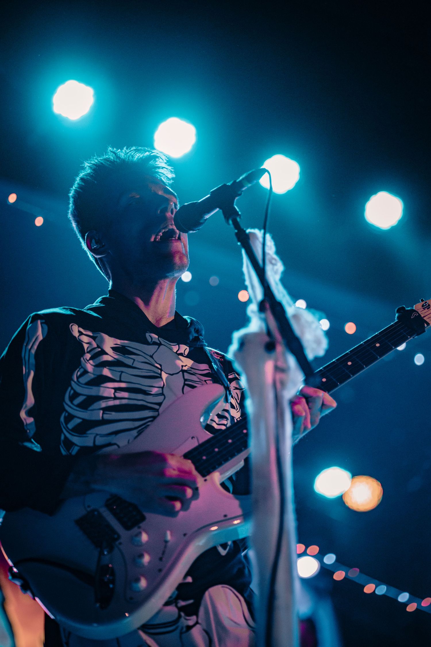 Musicians play electric guitars under moody blue stage lighting during a rock performance.