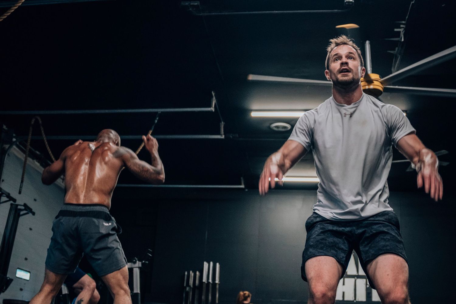 Athletes performing exercises in a dimly lit CrossFit gym with training equipment.