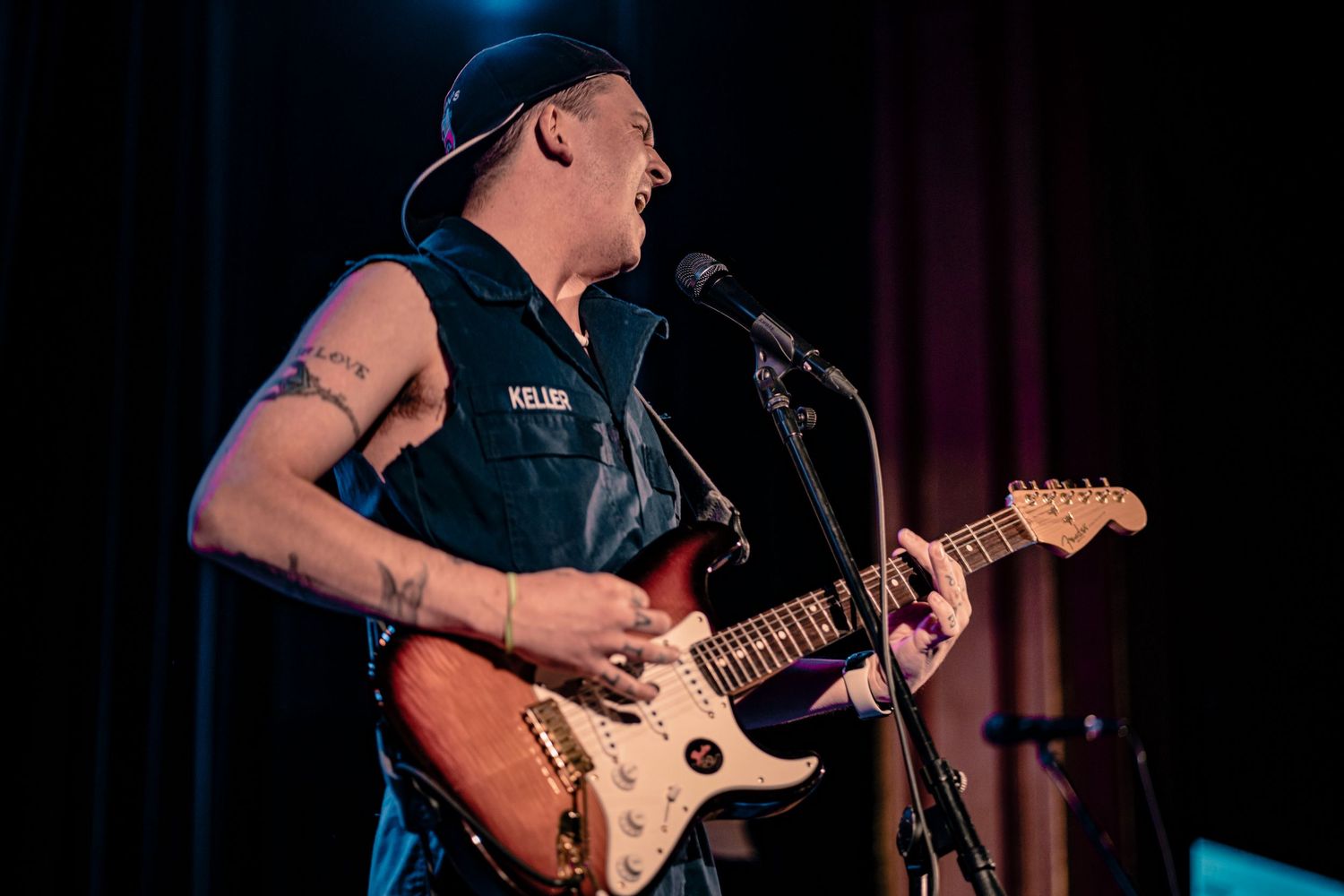 Guitar player performs energetically on stage with dramatic spotlighting.