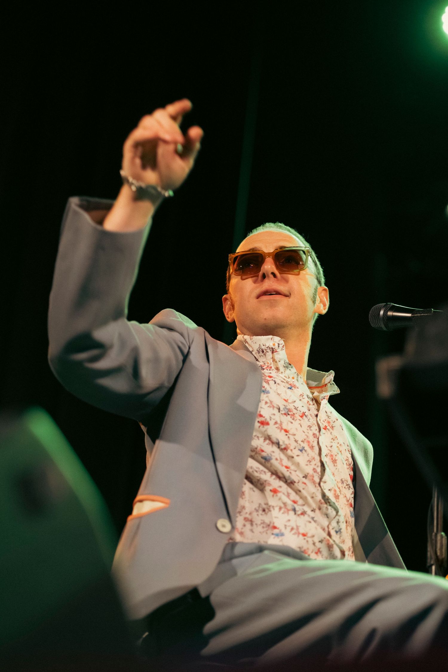 An animated performer in gray suit jacket gesturing enthusiastically during a stage performance.