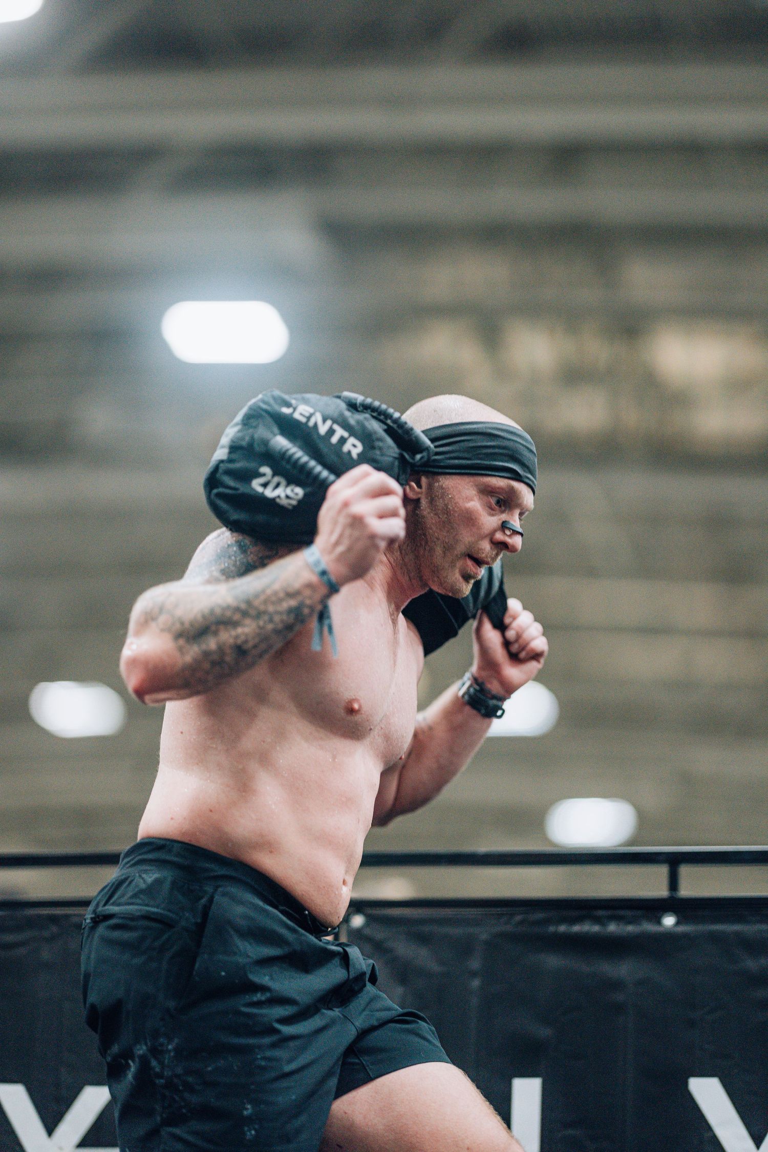 Athlete carrying a heavy sandbag during an indoor CrossFit competition.