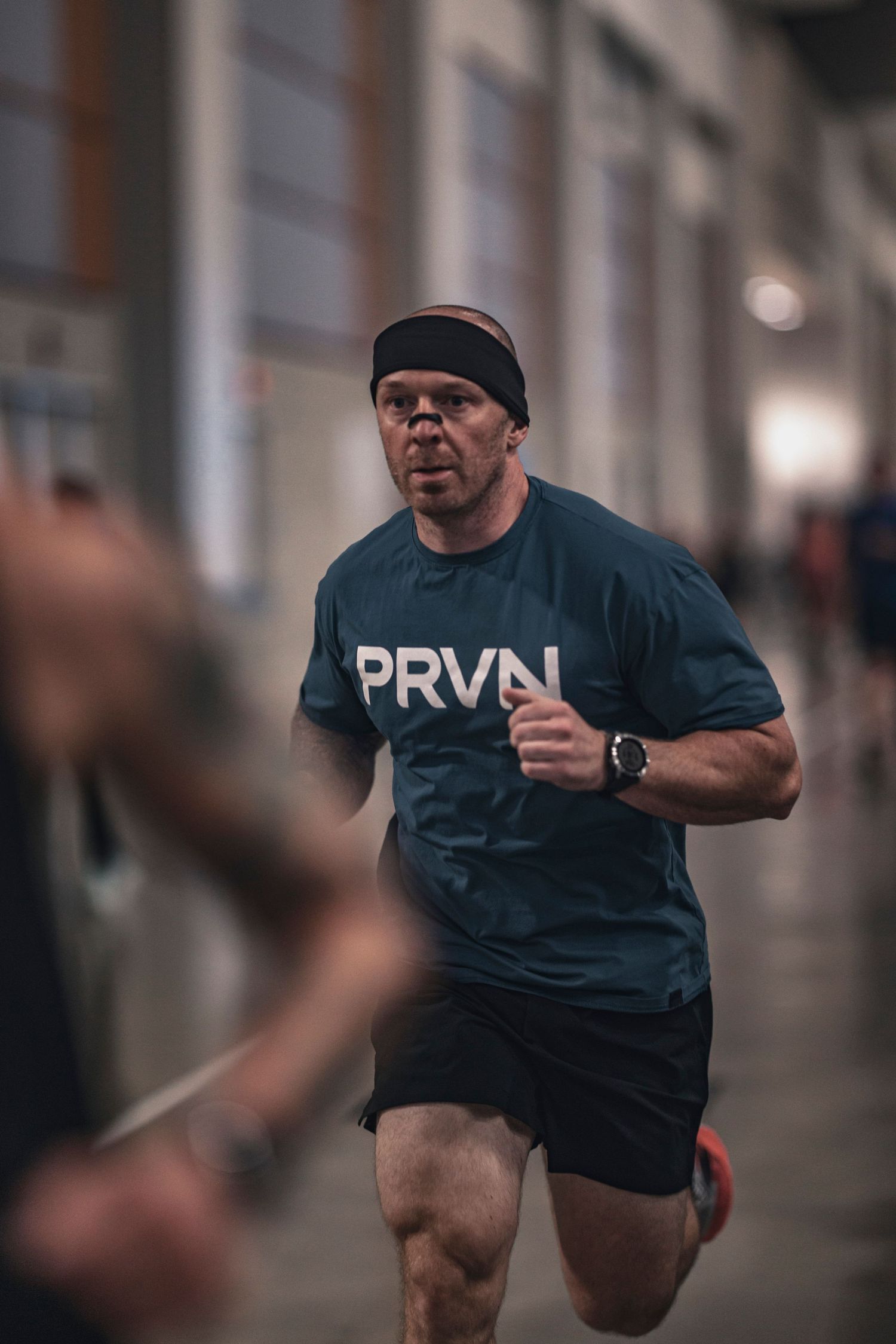 Athletic person in a PRVN shirt performing an intense workout movement in an indoor gym setting.