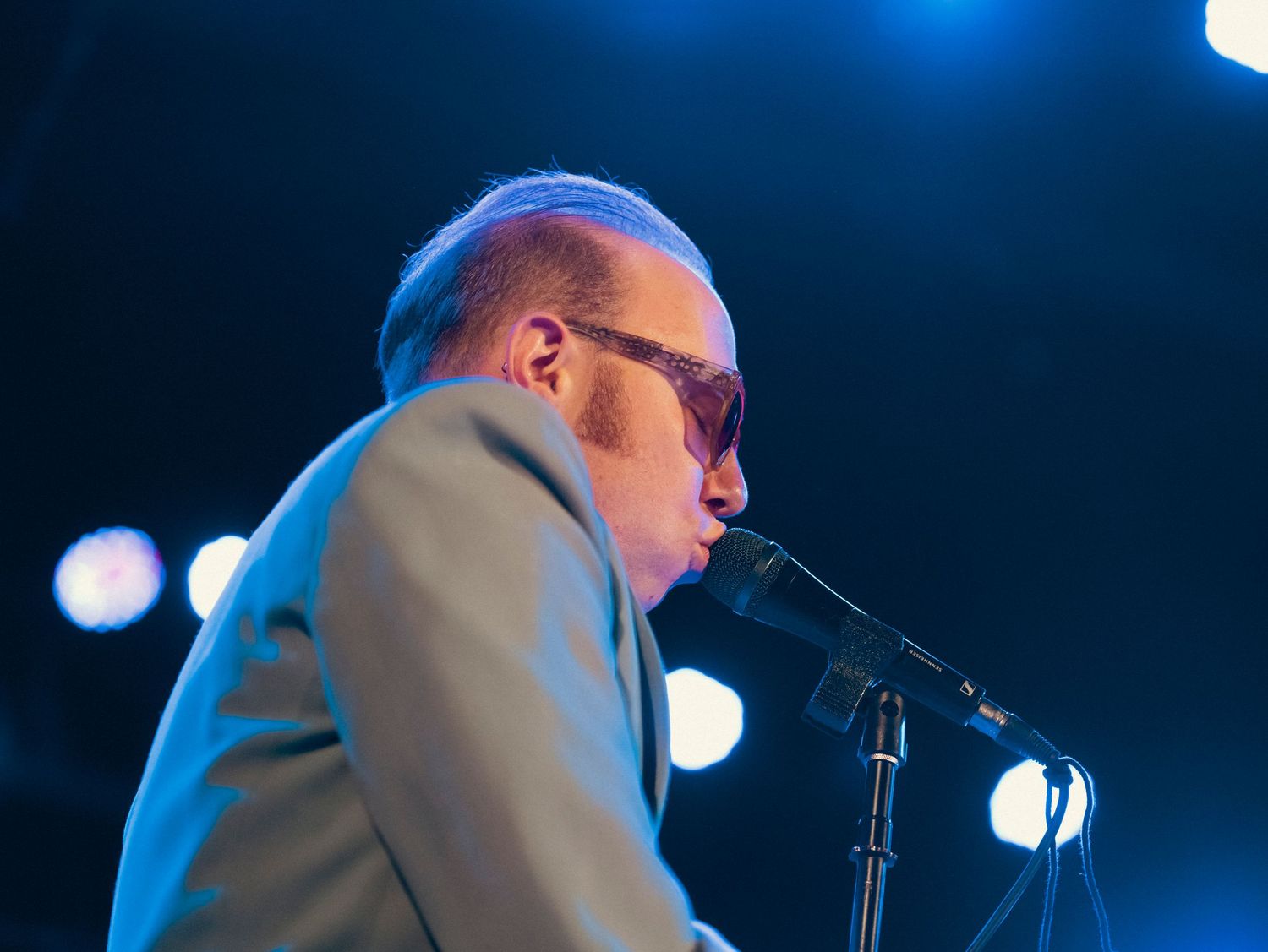 A musician performing under blue stage lighting with microphone stands visible.