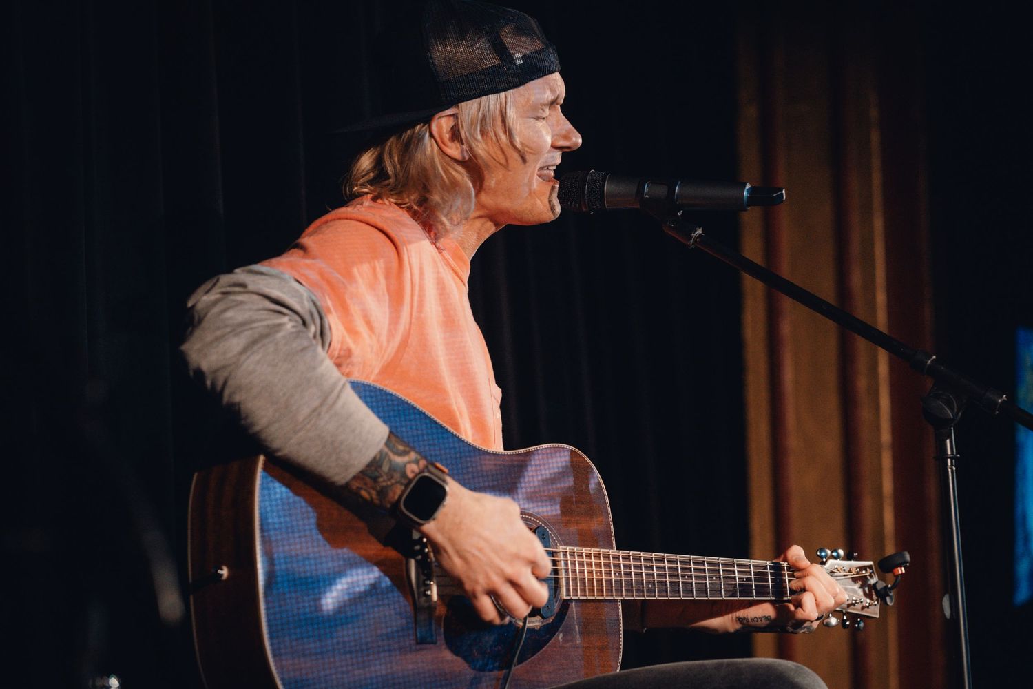 Musician in casual attire playing acoustic guitar during intimate venue performance.
