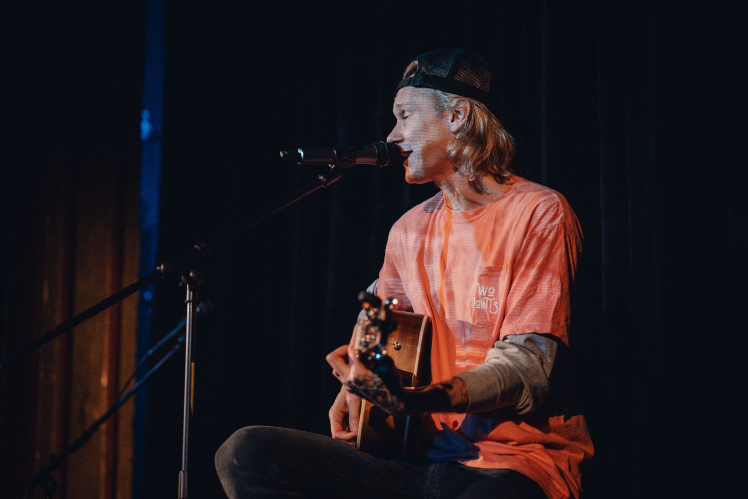 Performer in orange shirt on stage with blue lighting effects during concert.