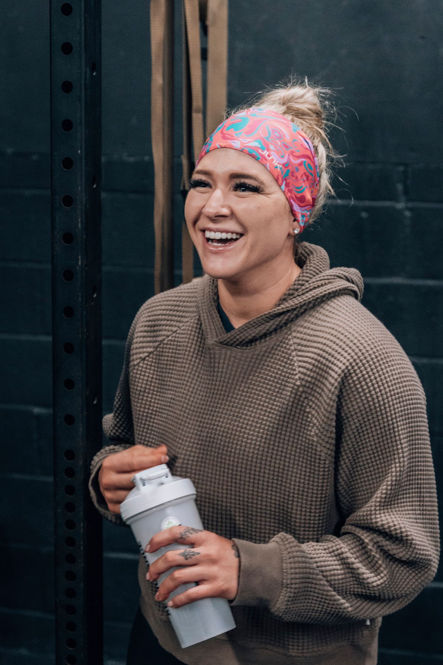 Person in brown knit sweater and colorful headband holding drink container.