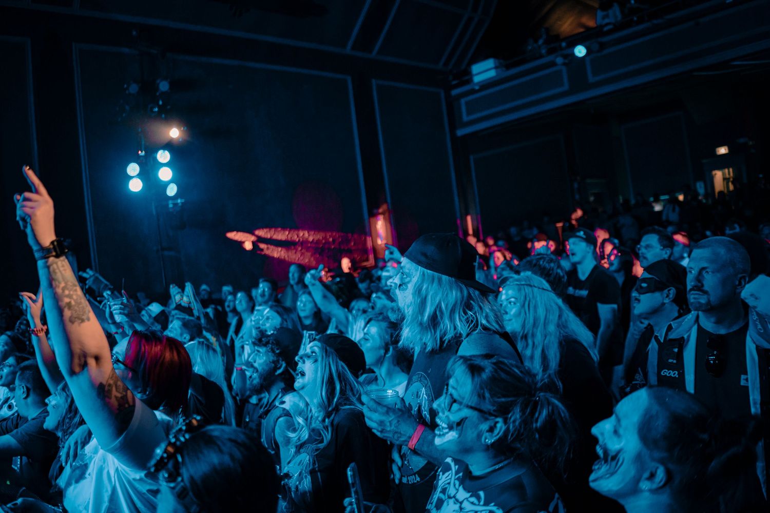 Concert crowd illuminated by blue lights raising hands during performance.