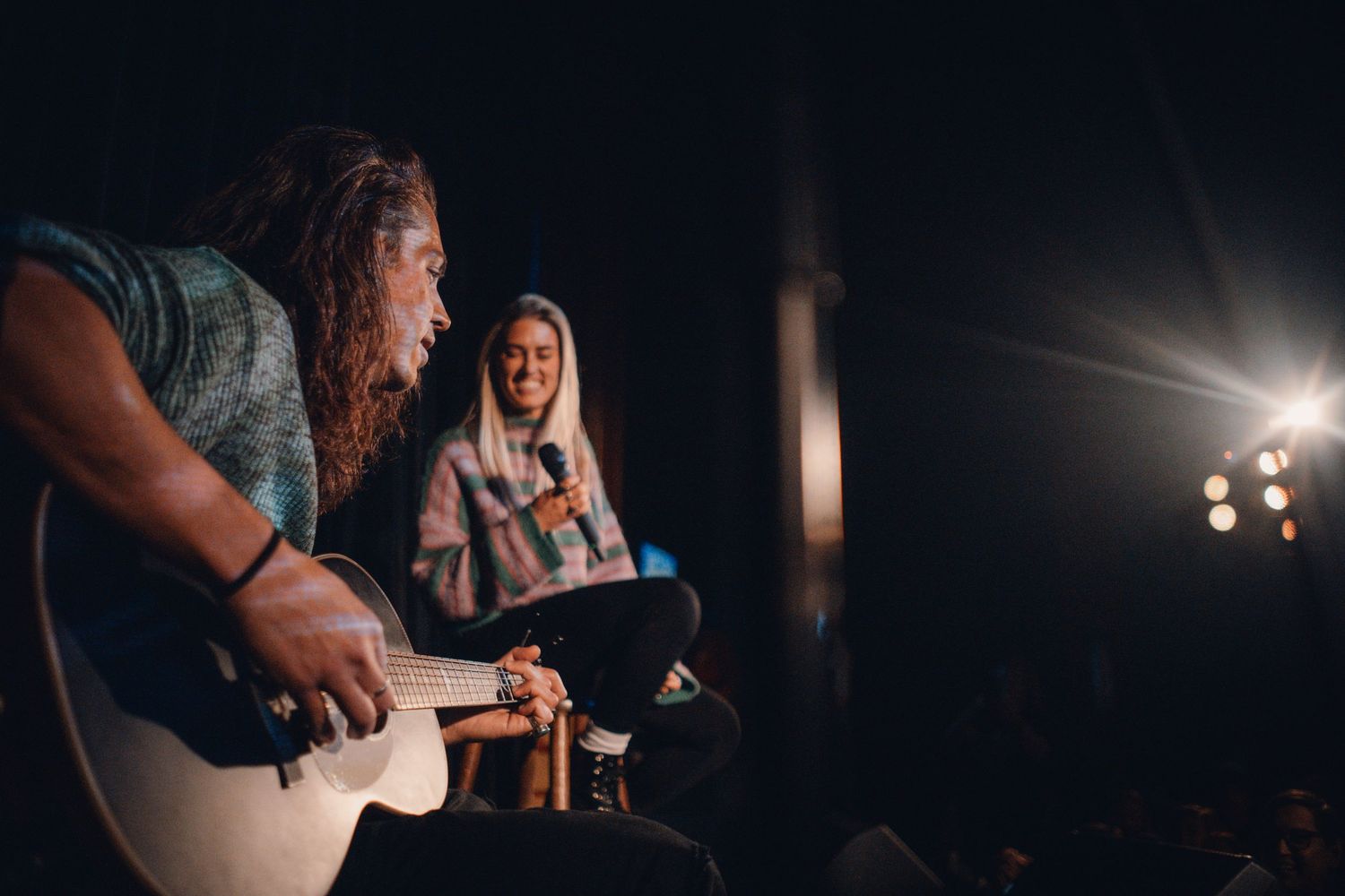 Musicians performing on stage with acoustic guitar under dramatic lighting.