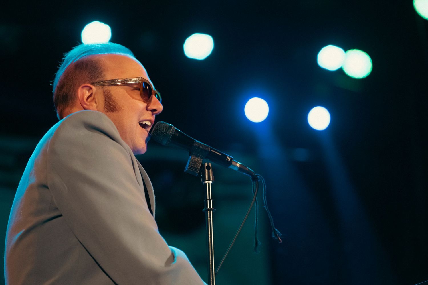 A musician performing at a piano under blue stage lighting.