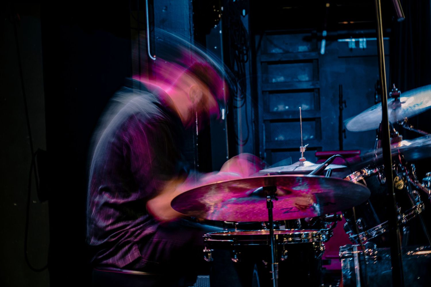 Drummer performs on stage with motion blur effect under dramatic red lighting.