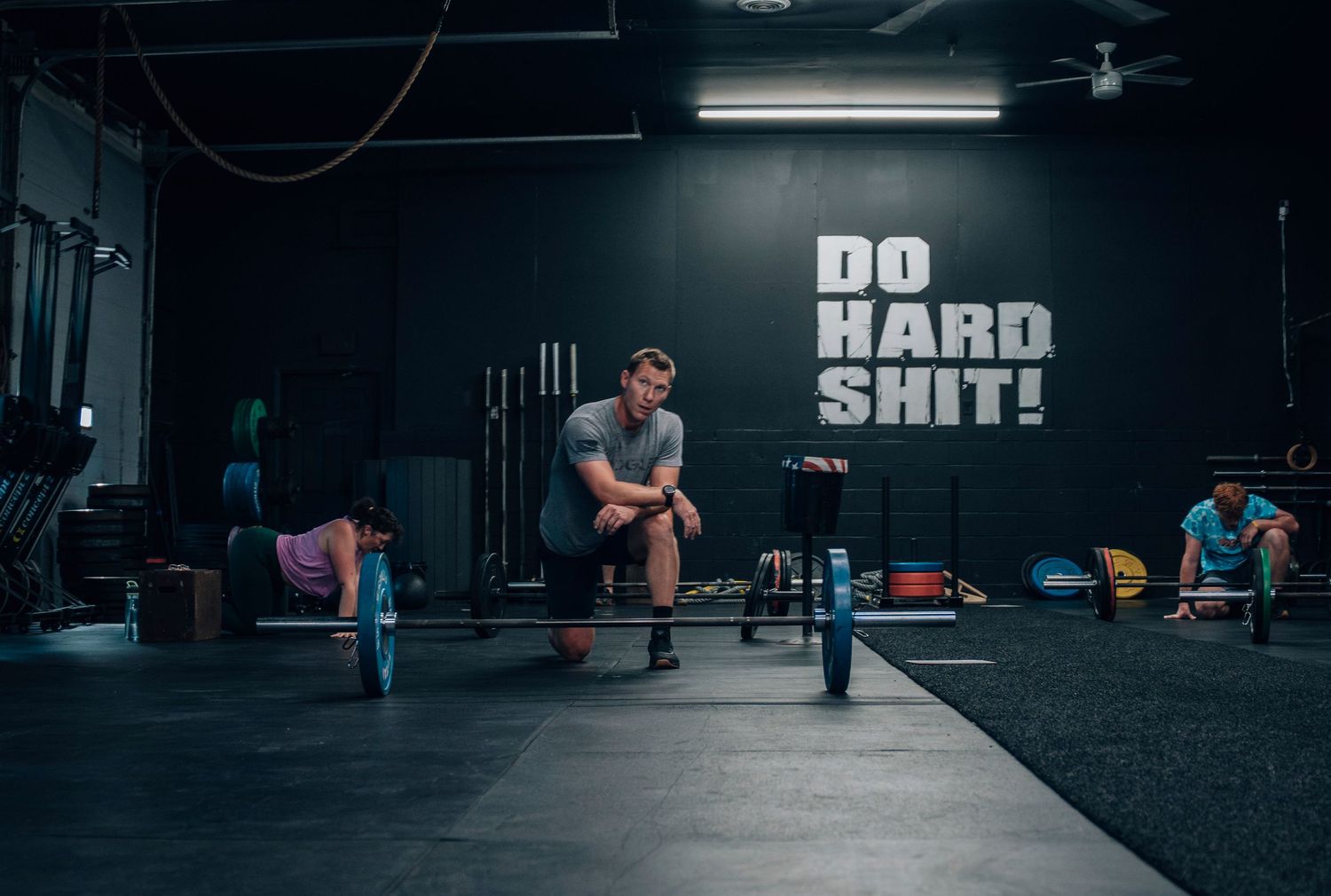Dark interior of a CrossFit gym with workout equipment and motivational text on walls.