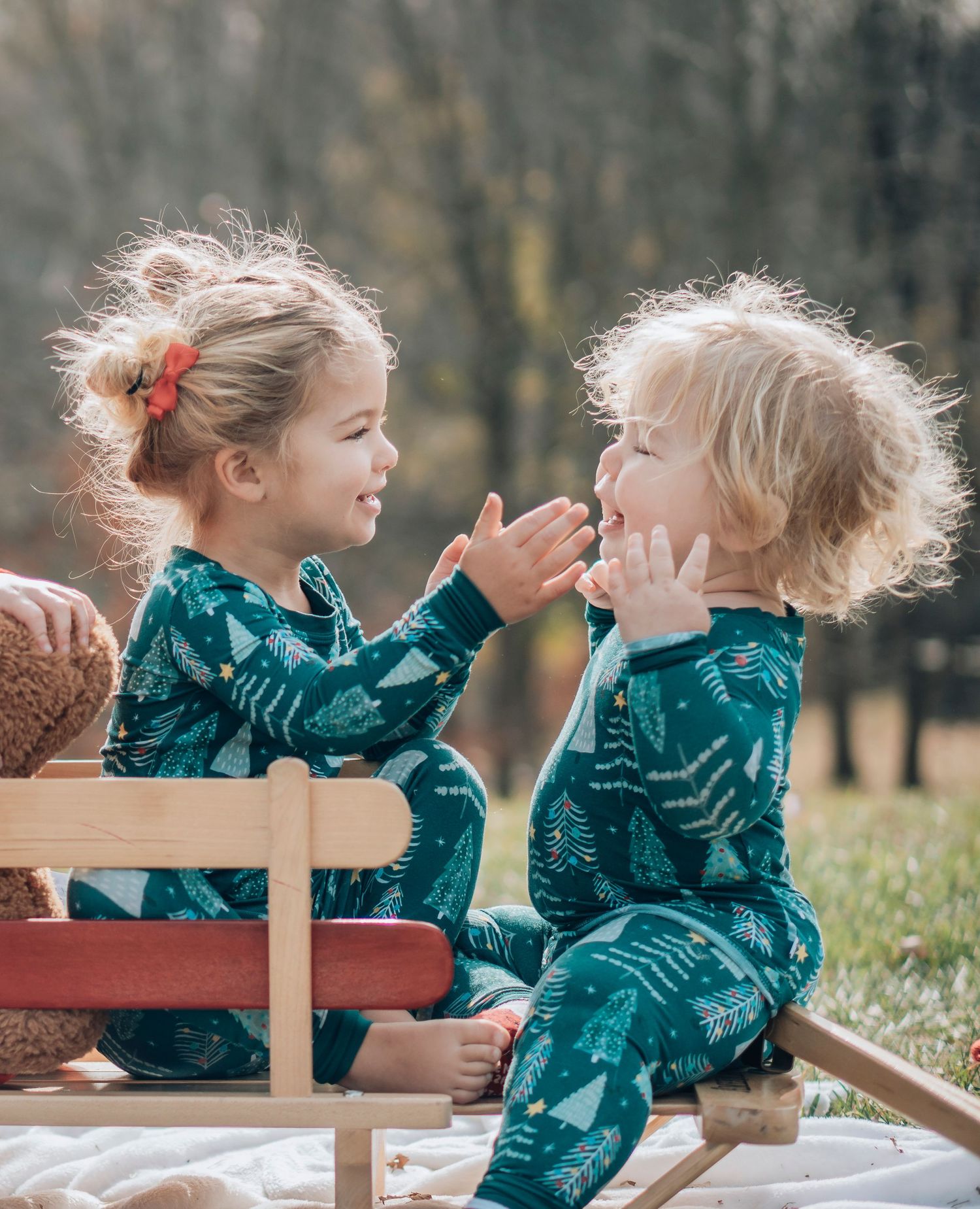 Two children in matching teal outfits share a playful moment on a wooden bench outdoors.