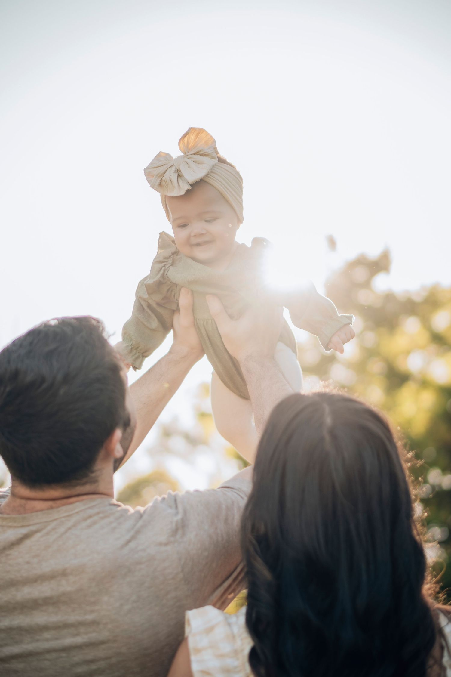 A parent lifts a small child into the sunlit sky during a joyful outdoor moment.