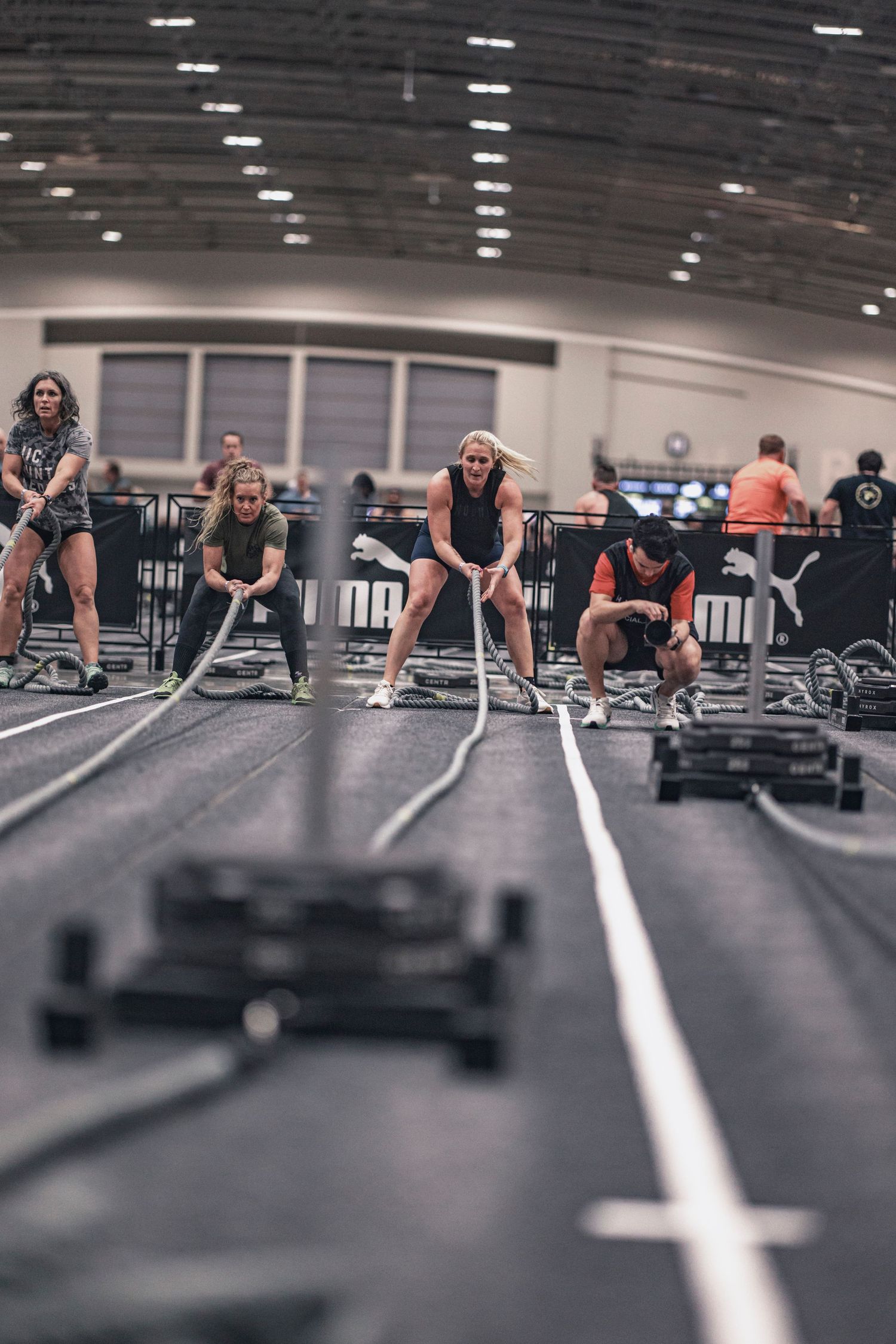 Group workout session in a spacious gym with equipment and floor markings visible.