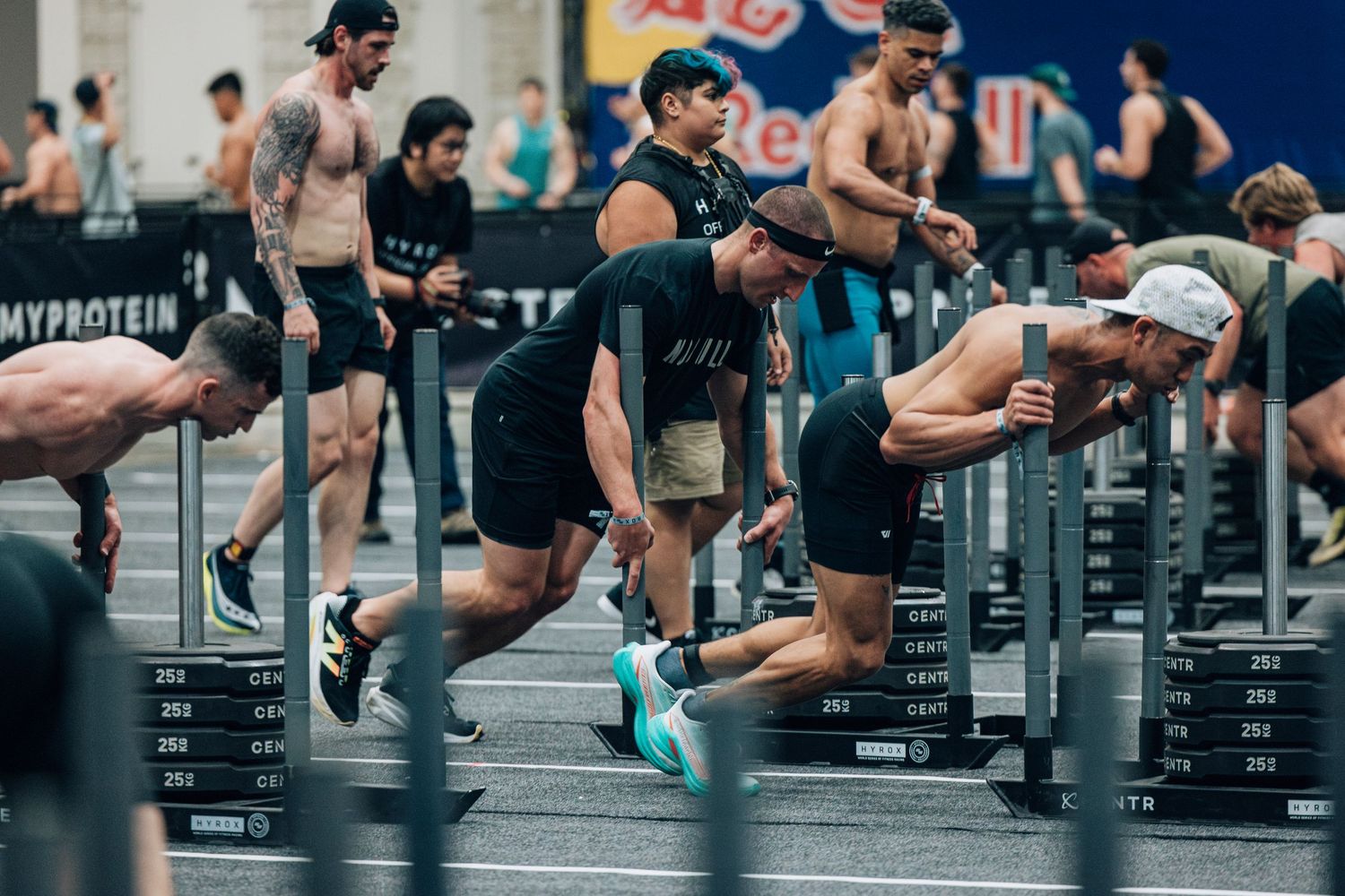 Athletes perform intense sled push exercises during a competitive fitness event.