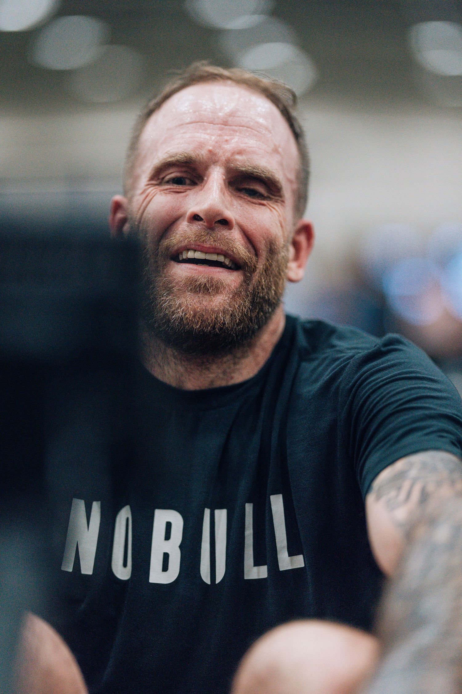 Athletic person wearing a black 'NO BULL' t-shirt smiling at the camera during a workout session.