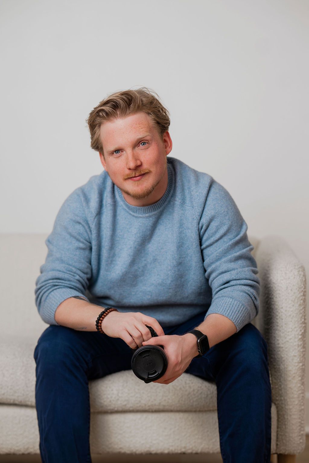 Person wearing blue sweater sitting on light colored couch in minimalist setting.