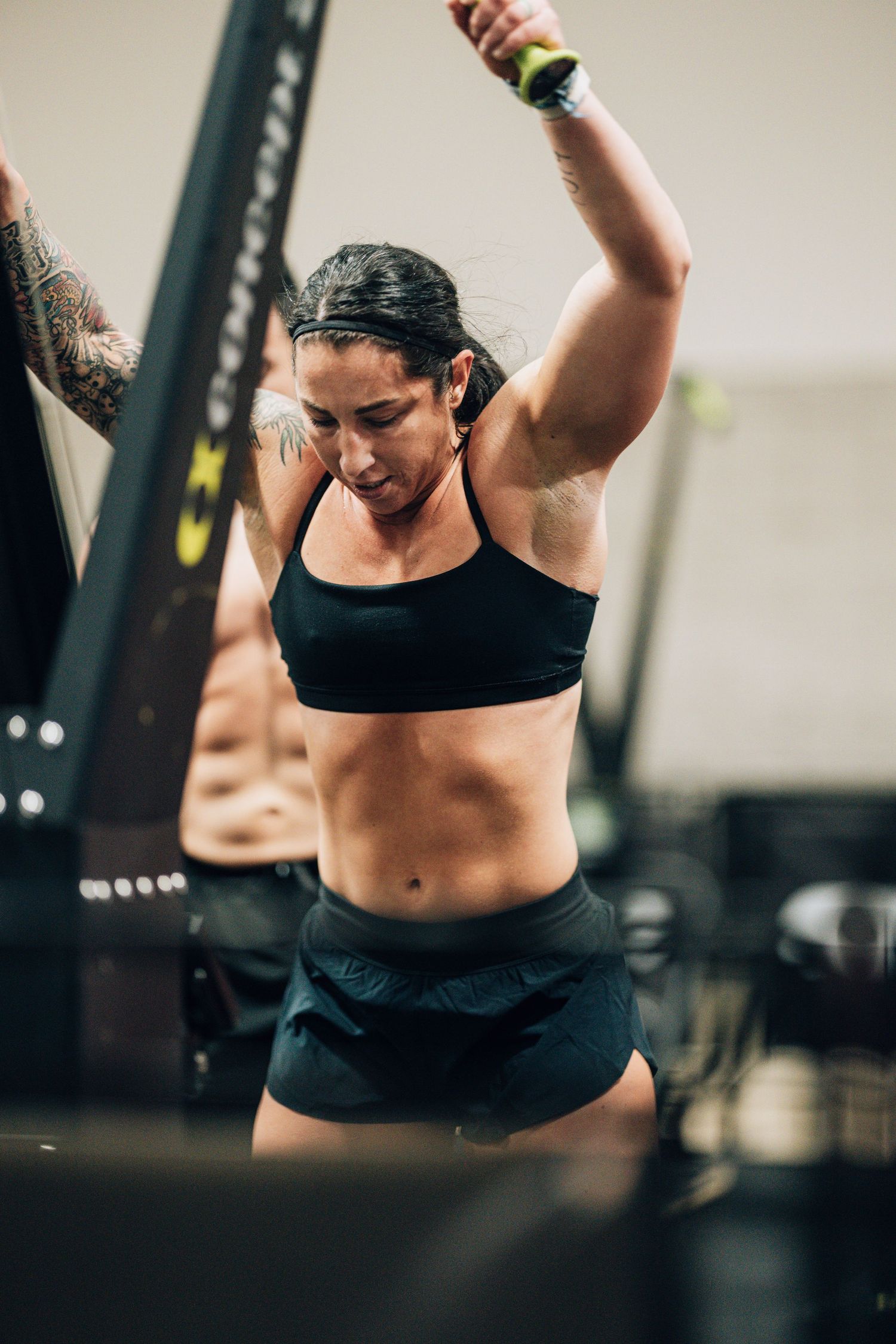 Athlete in black sports attire performing an overhead exercise during intense workout.