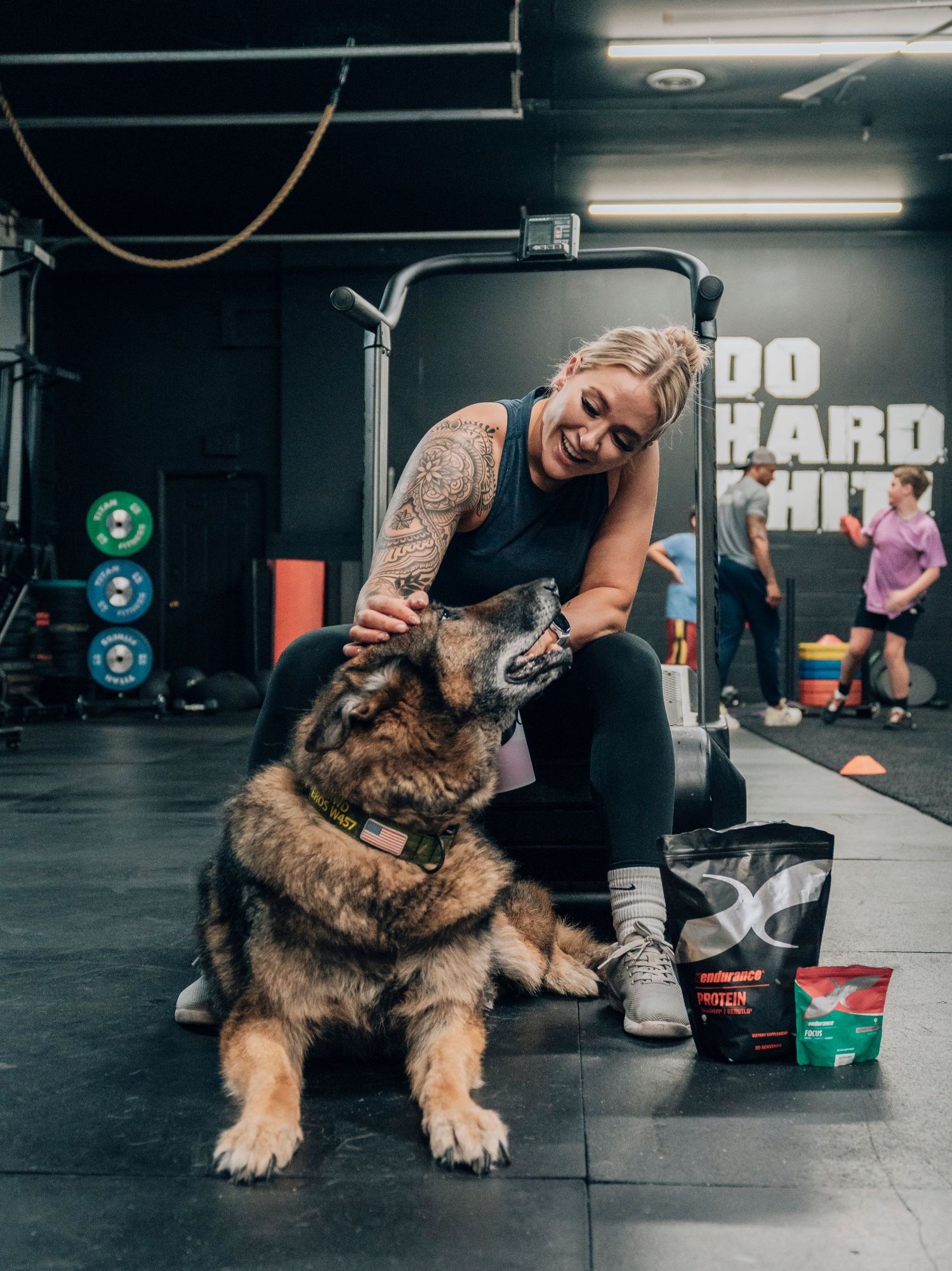 Athlete petting large German Shepherd dog while resting at gym.