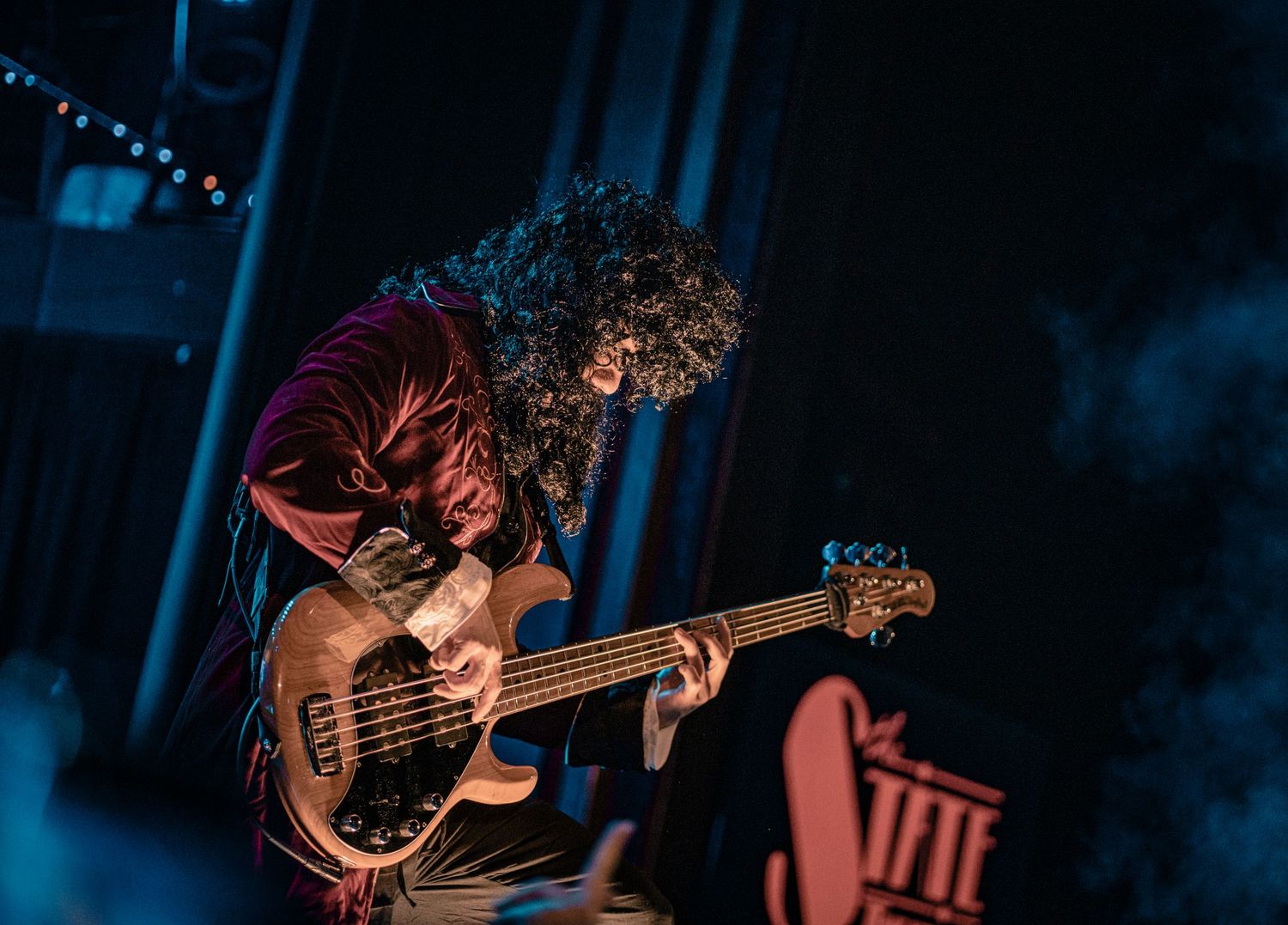 Bass guitarist plays instrument during dimly lit concert performance.
