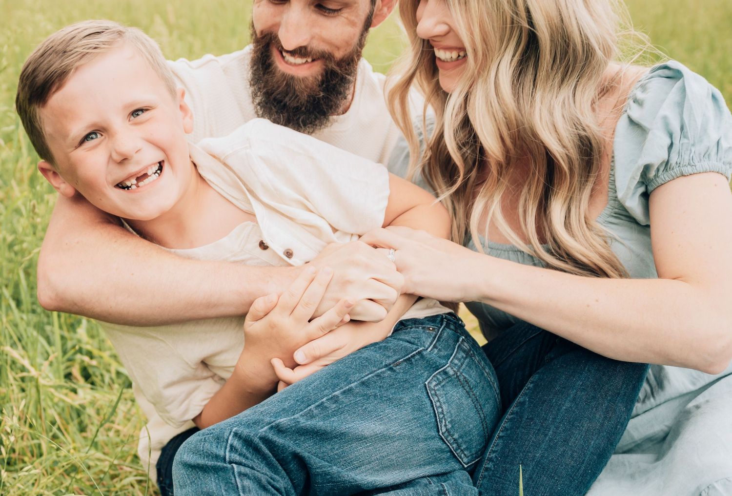 A joyful family shares a tender moment together while sitting in a sunny grass field.
