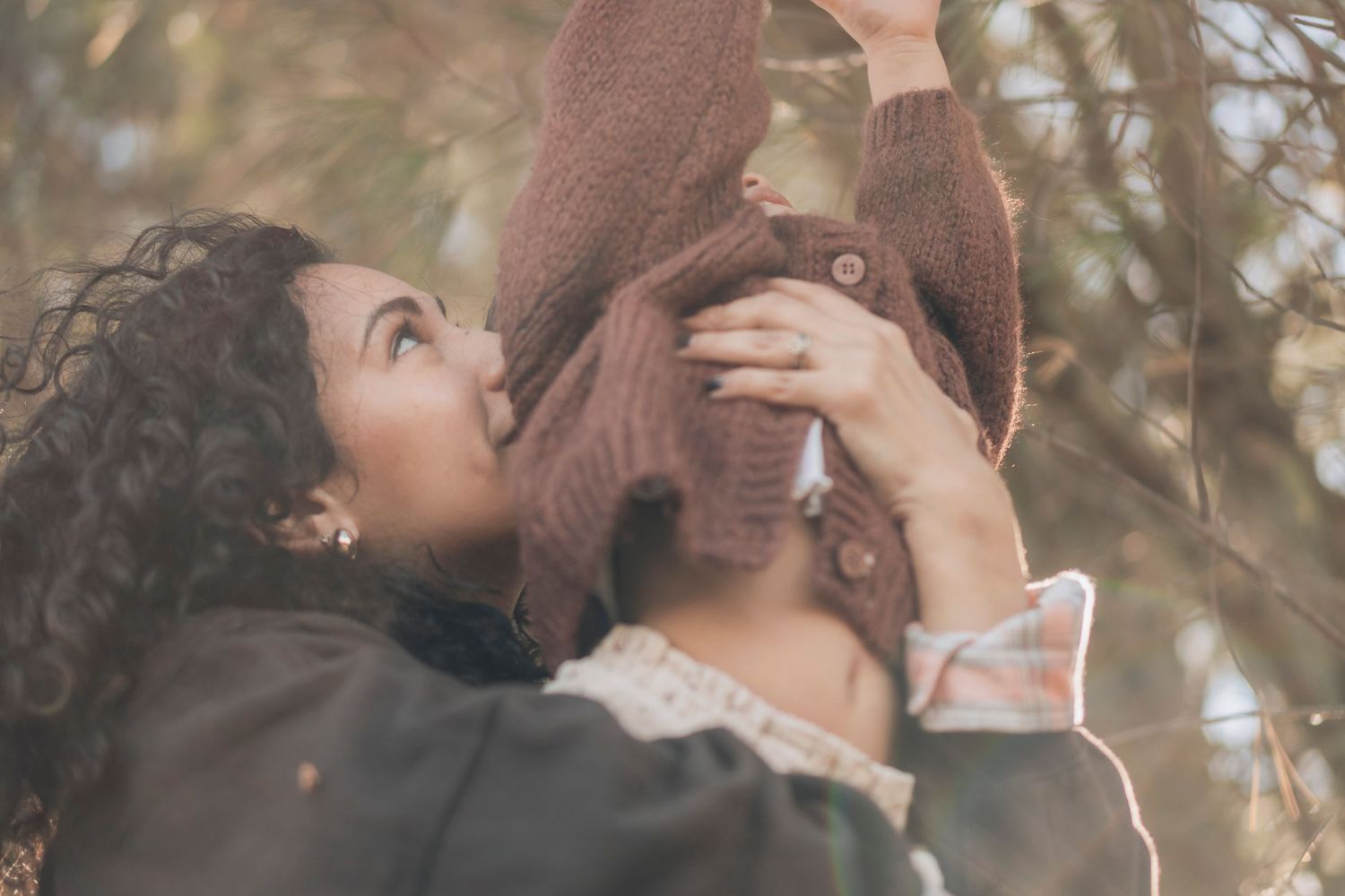 A couple shares a tender romantic kiss outdoors in a natural setting with sunlight filtering through trees.