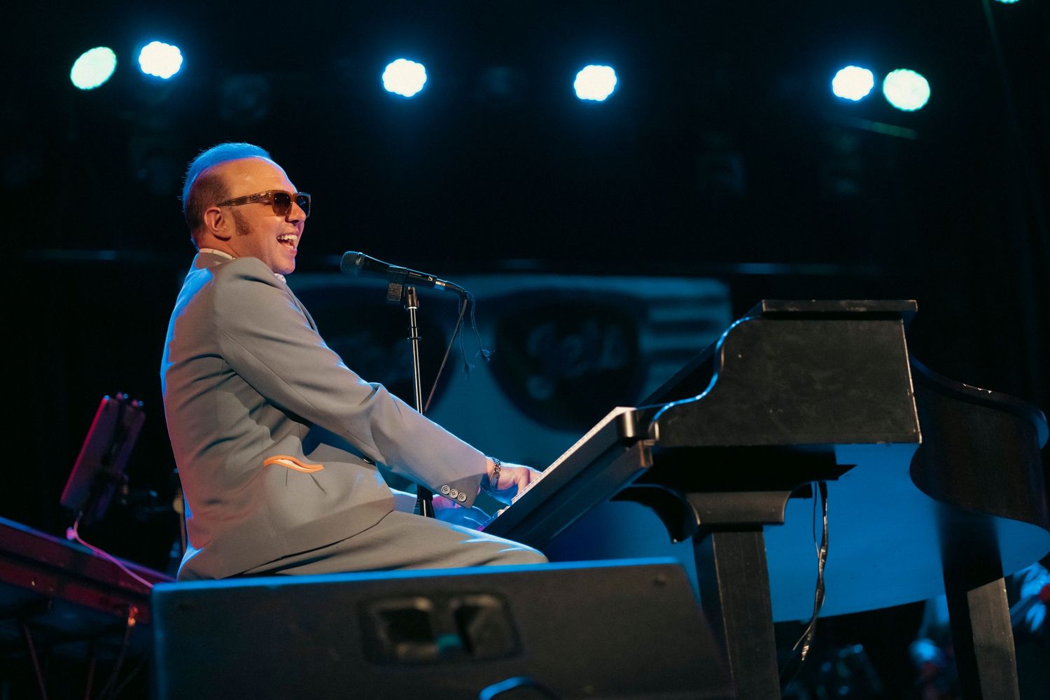 A musician performing at a piano under dramatic blue stage lighting.