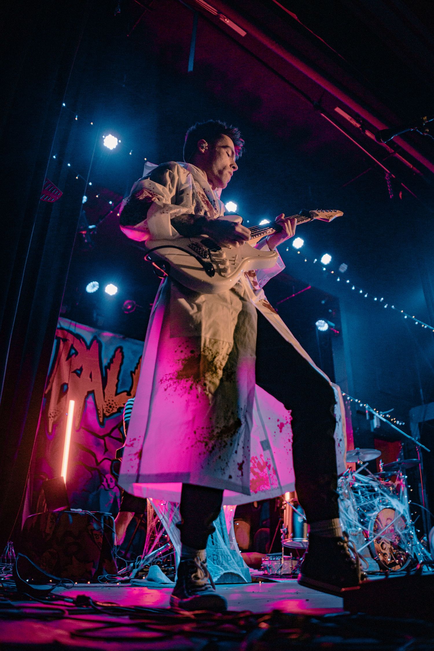 Rock band performs on stage with vibrant pink and blue lighting effects.