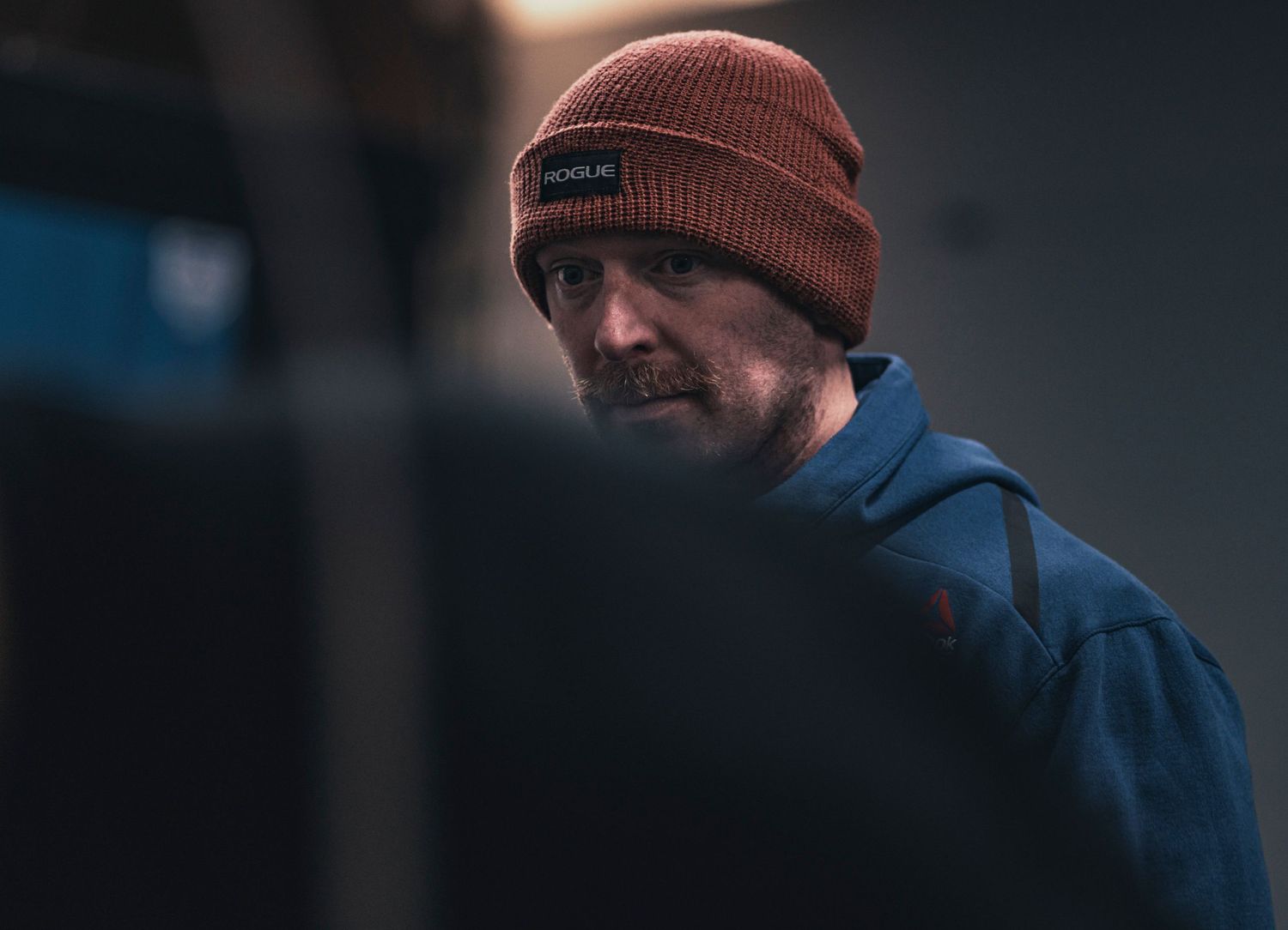 Person wearing an orange beanie against a dark background in moody lighting.