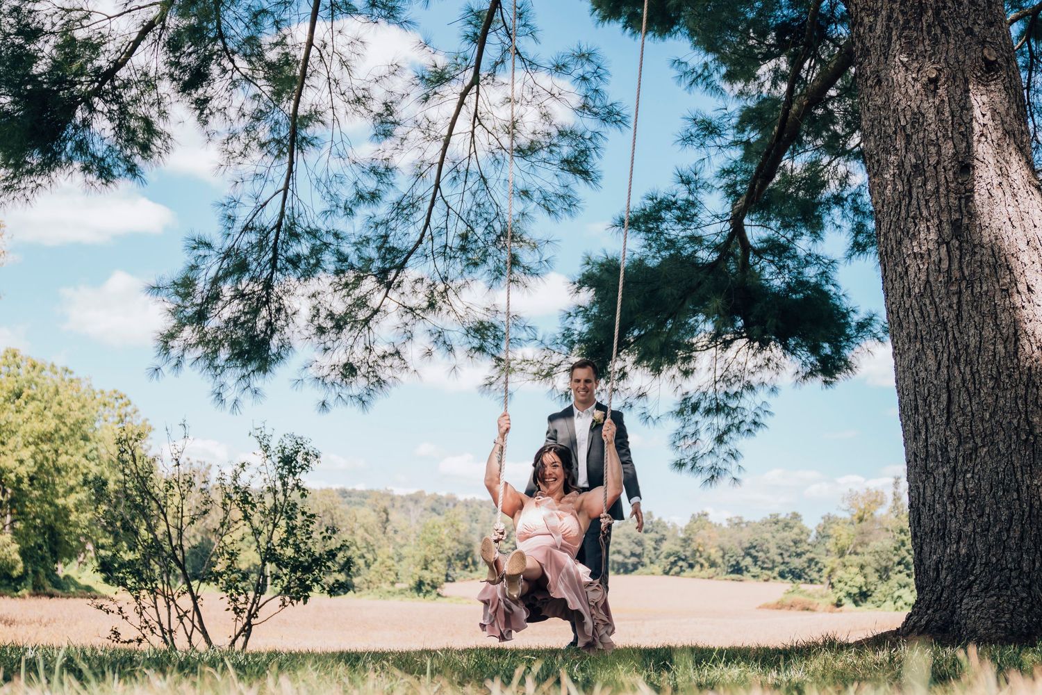 A couple enjoys a romantic moment on a tree swing in a sunny park setting.